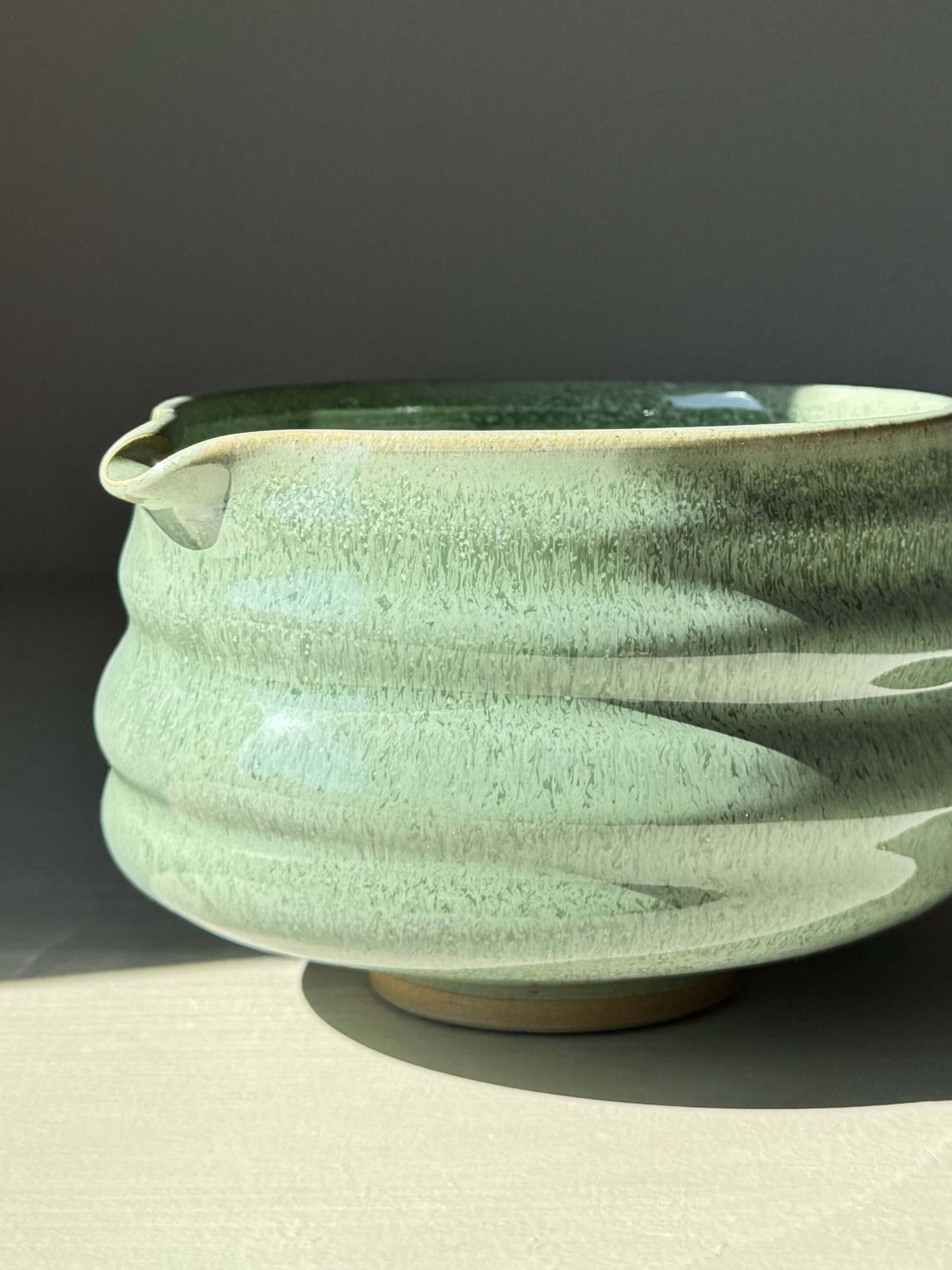 Close-up of a sage-glazed matcha bowl with spout, featuring ridged design and glossy finish, perfect for enhancing matcha preparation.