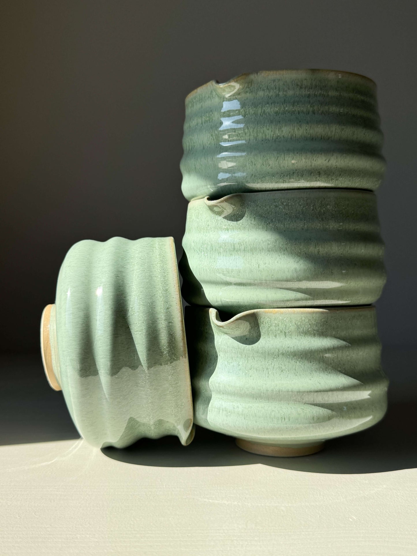 Stack of green Matcha bowls with spouts featuring sage glaze and ridged design on a light background.