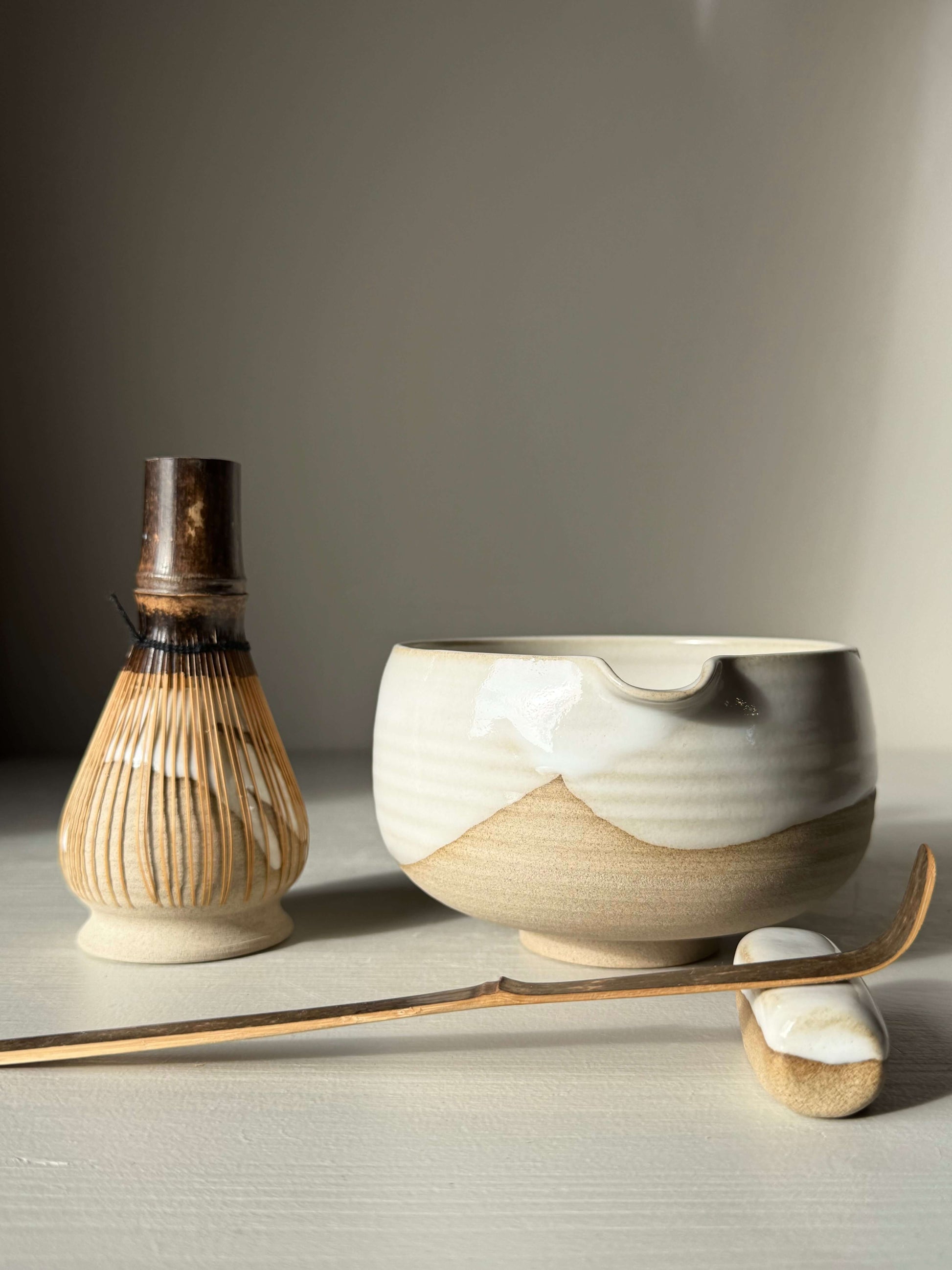 Handmade ceramic Matcha Bowl with Spout – Yuki #03, featuring toffee clay and glossy white glaze, alongside a traditional bamboo whisk.