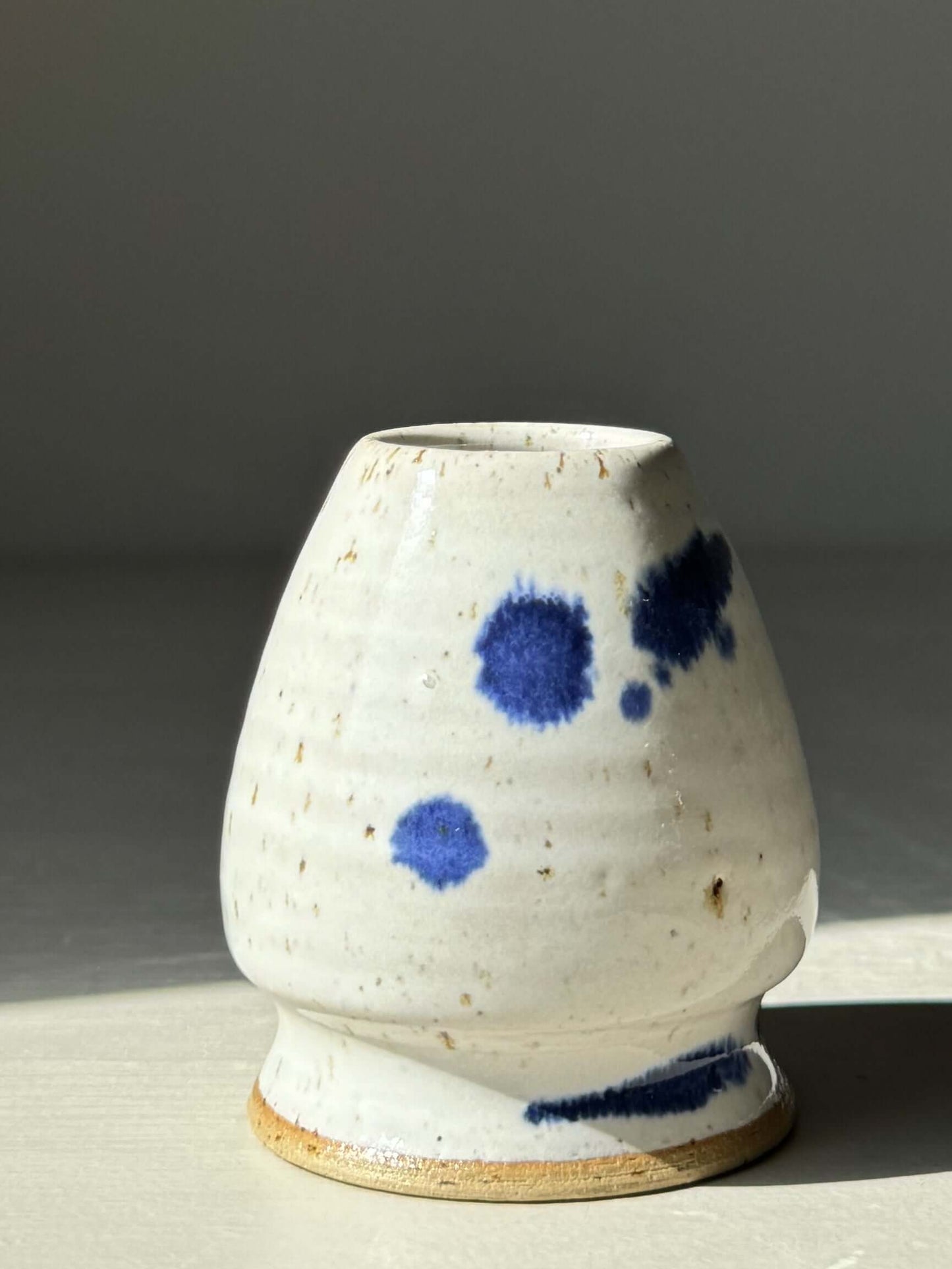 Hand-thrown matcha whisk holder in glossy white glaze with cobalt blue splashes, designed to preserve whisk shape.