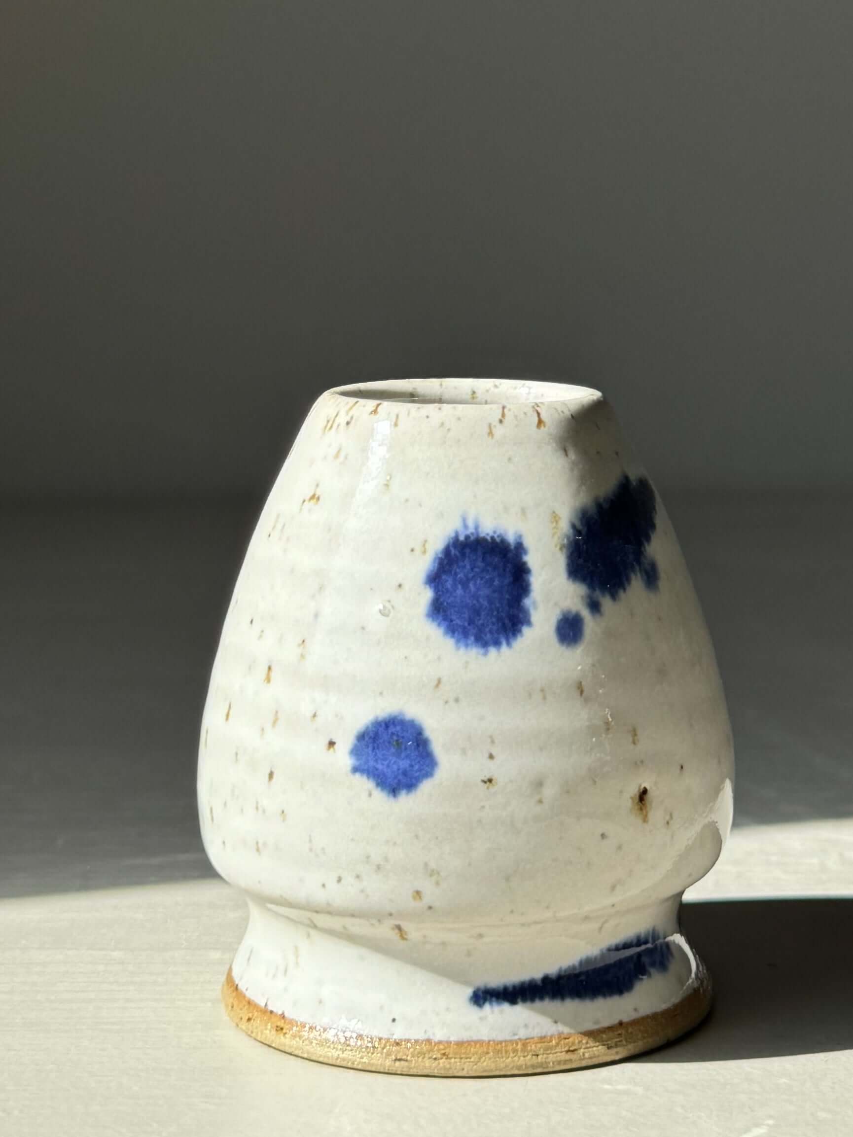 Hand-thrown matcha whisk holder in glossy white glaze with cobalt blue splashes, designed to preserve whisk shape.