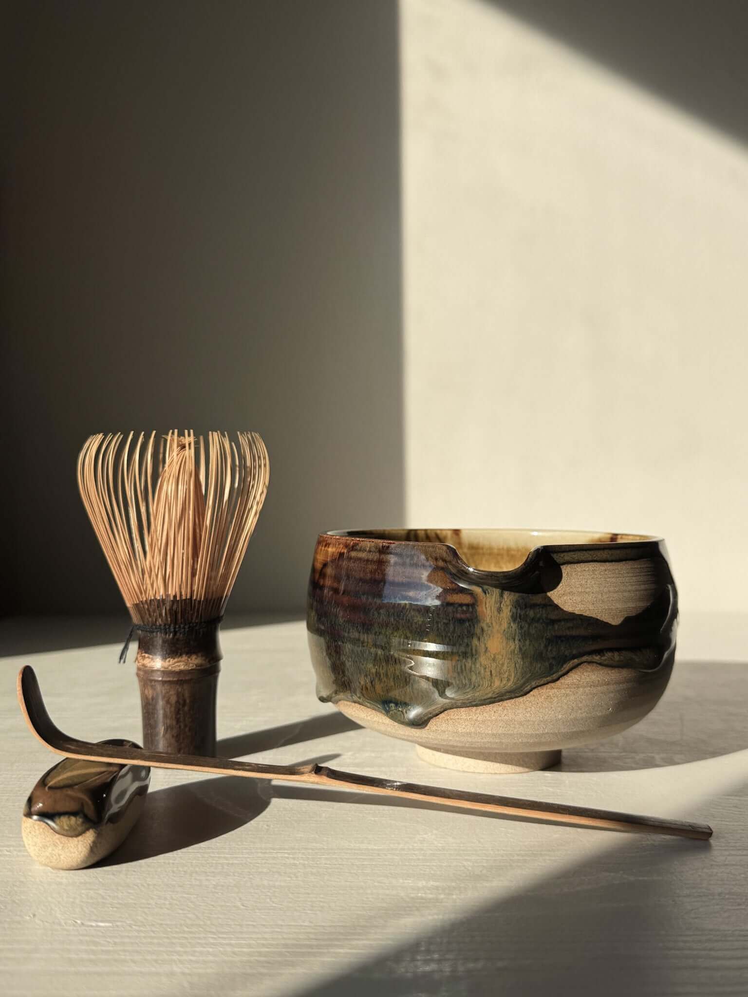 Handmade ceramic Matcha Bowl with Spout – Inyo #06 featuring unique glaze, beside a whisk and matcha spoon on a light background.