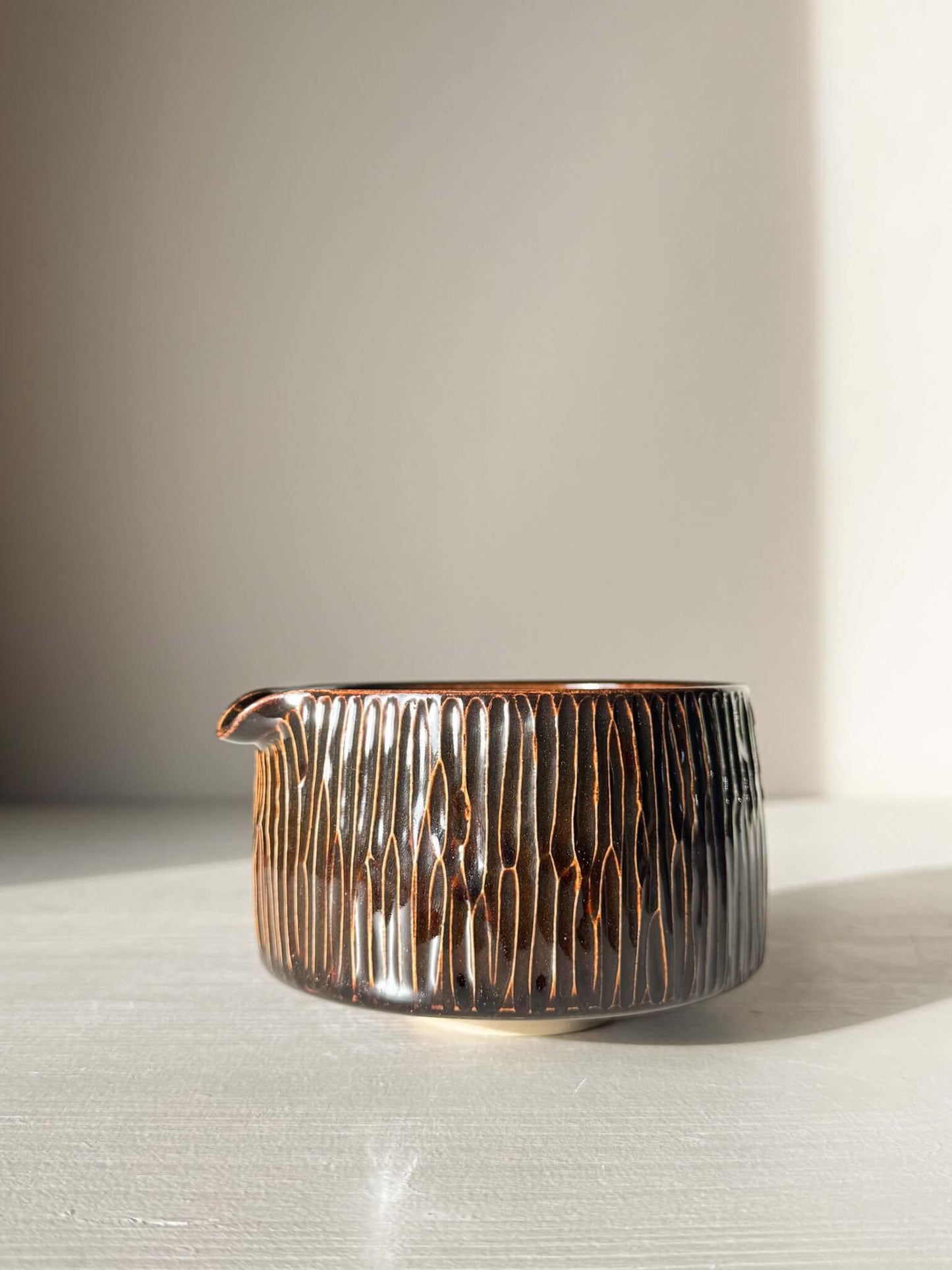 Matcha Bowl Spout – Kinsei #01 with hand-carved vertical lines and glossy glaze, deep brown and golden highlights, on display.