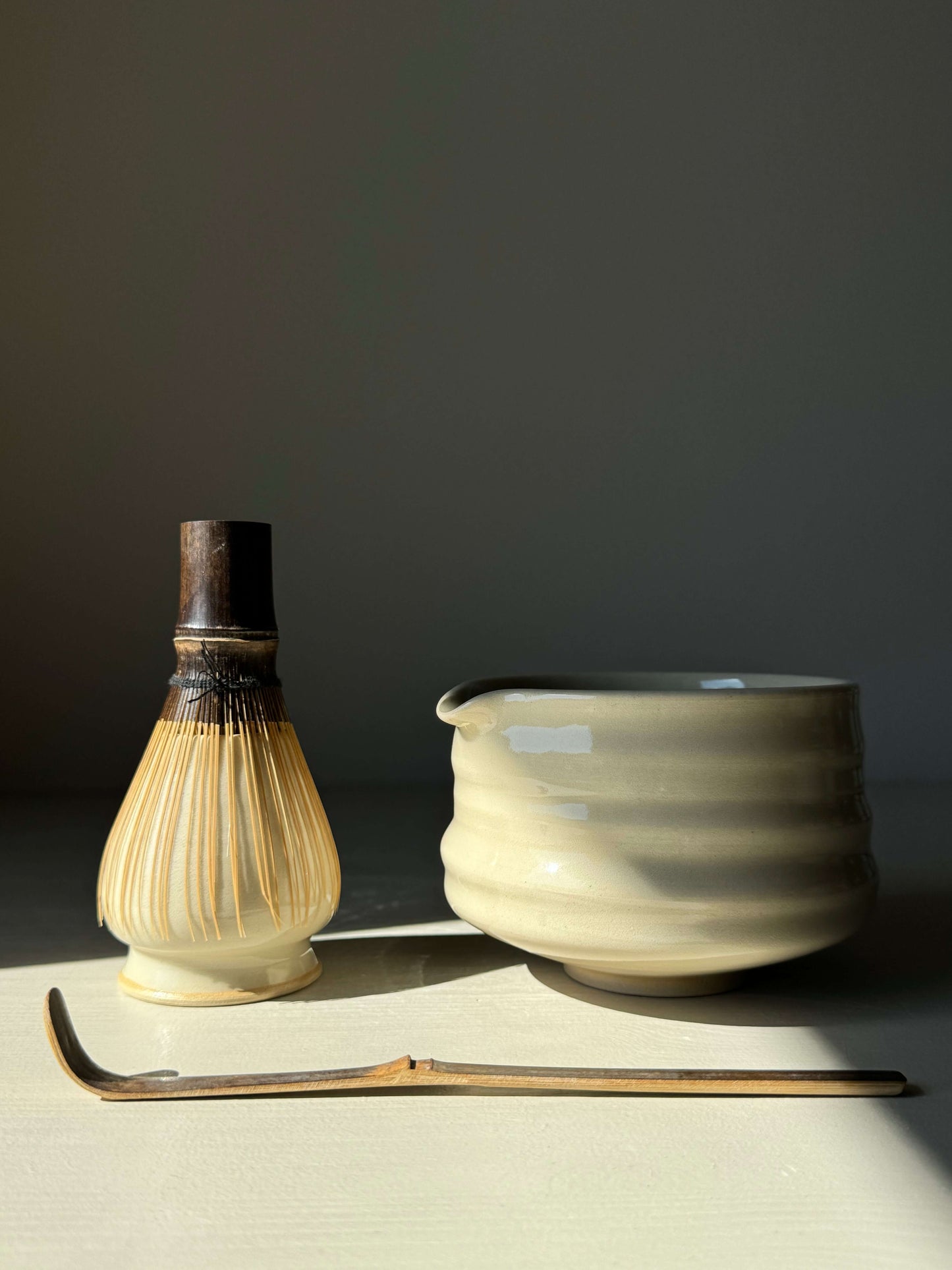 Matcha bowl with spout in clear glaze alongside bamboo whisk and scoop for traditional tea preparation.