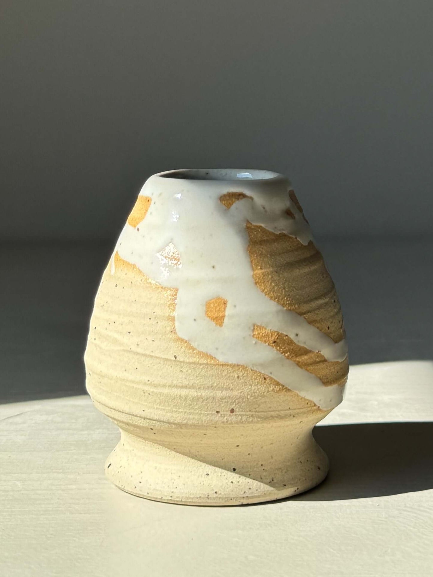 Matcha whisk holder with glossy white glaze over speckled clay, showcasing warm earthy tones peeking through for added depth.