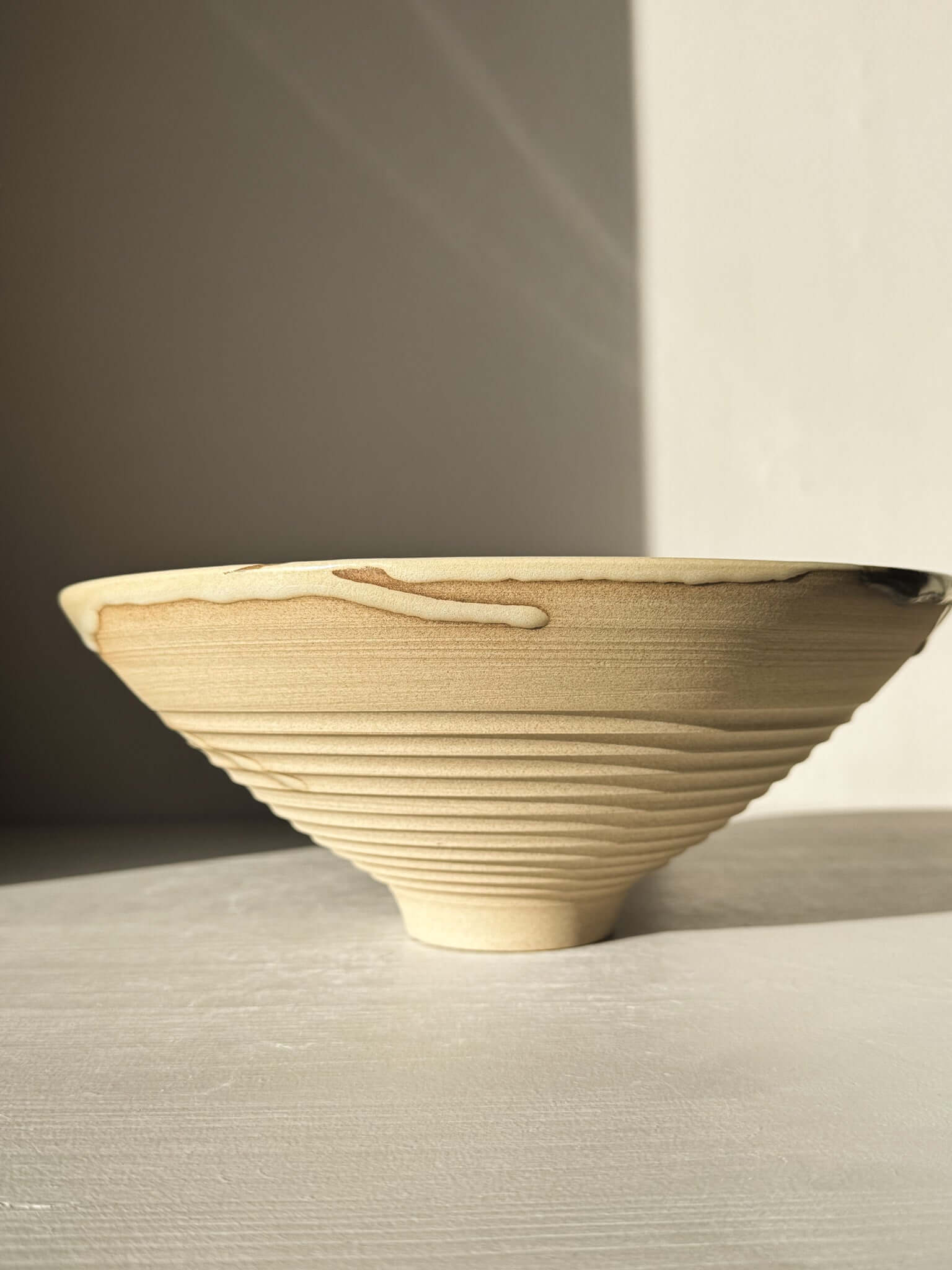 Medium Carved Bowl - Inyo #02 with sculptural carved exterior and flowing glaze drips on raw clay surface, side view.
