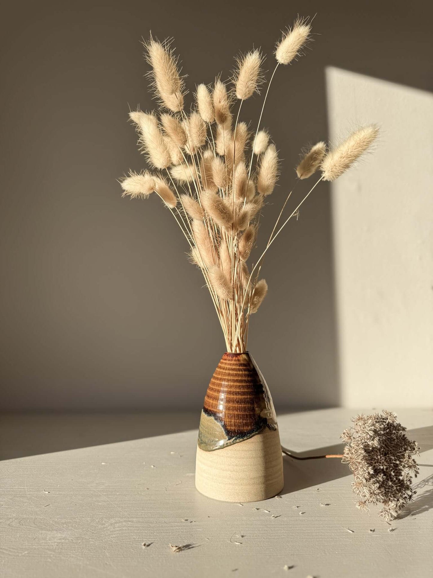 Medium Vase – Inyo #02 with soft curves and tenmoku glaze holding dried grasses on a sunlit surface.