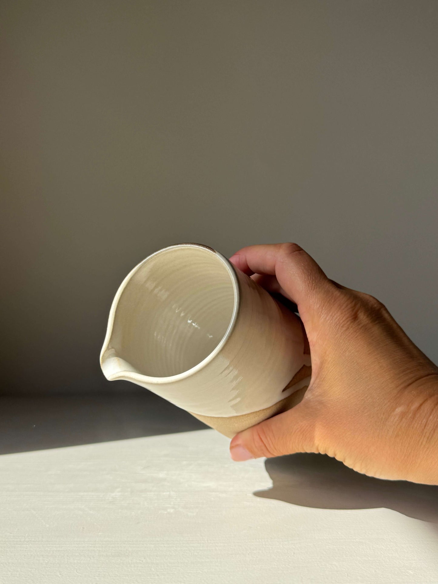 Hand holding a Medium Vase / Jug – Yuki in white glazed handmade ceramic, showcasing its elegant sculptural design and toffee-colored clay base.