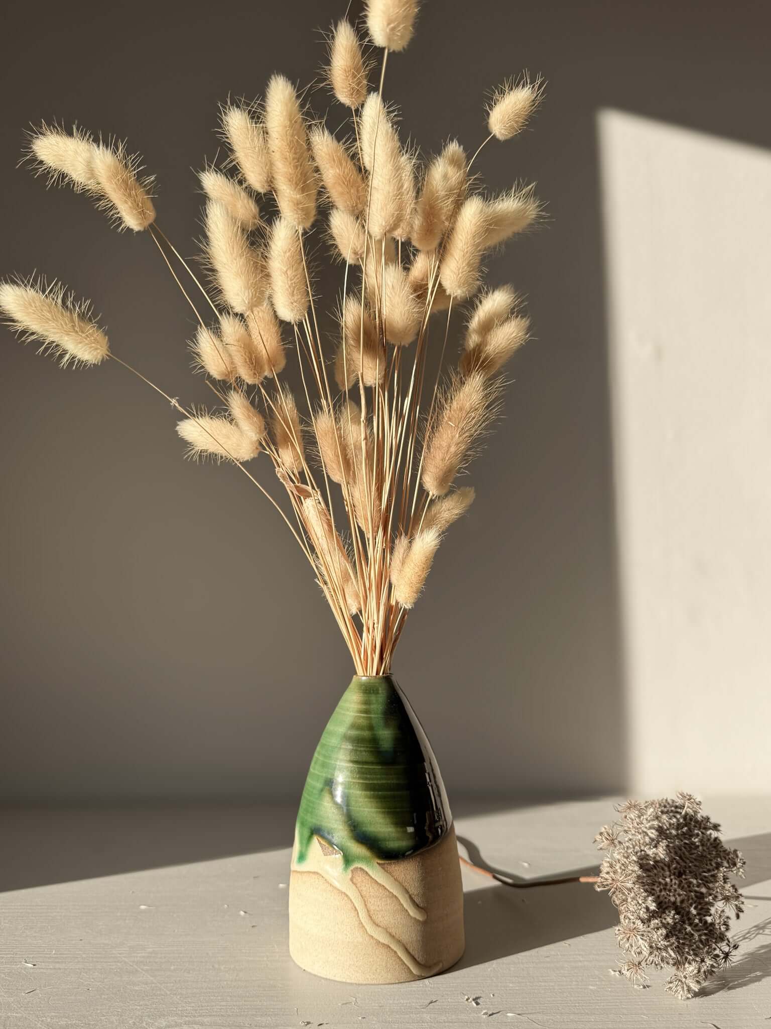 Medium Vase – Mori #01 with natural green glaze and earthy tones, featuring dried grasses, perfect for home decor on a sunlit surface.