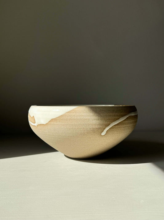 Medium bowl from Yuki Series with white glaze and toffee clay, showcasing a conical shape and raw texture, bathed in natural light.