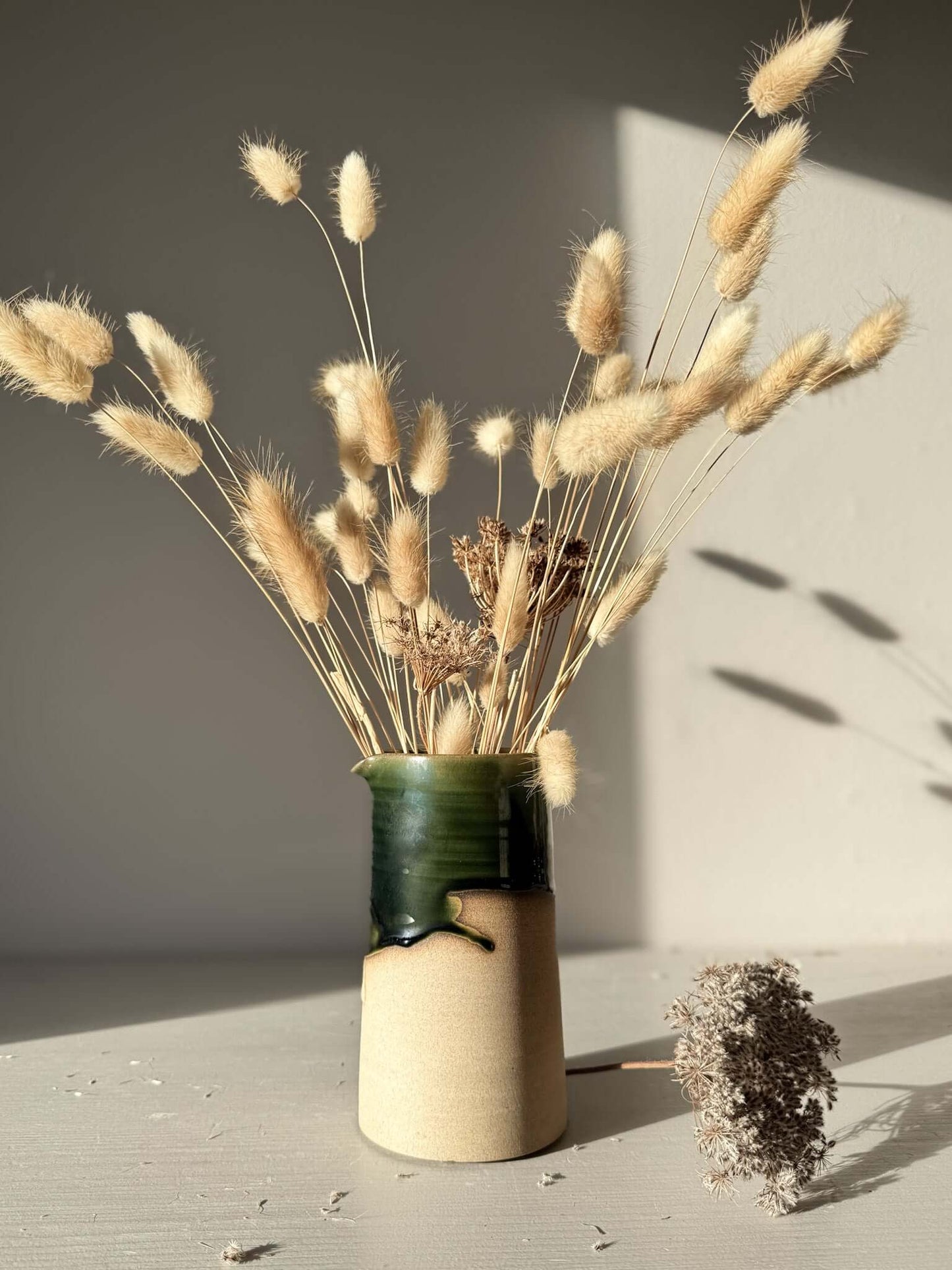 Medium Vase/Jug – Mori #01 with dried flowers, showcasing a glossy green glaze and raw clay base in sunlight.