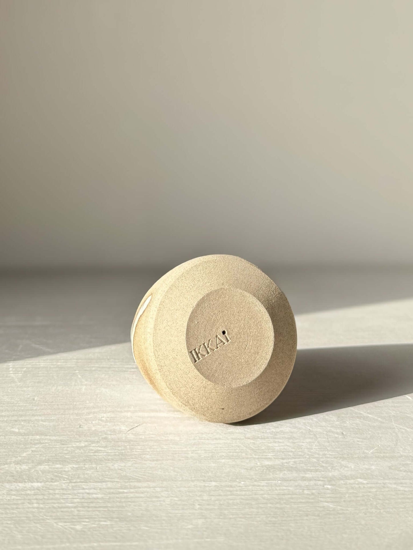 Base of a handmade ceramic item with engraved logo, displayed on a white surface with soft natural lighting.