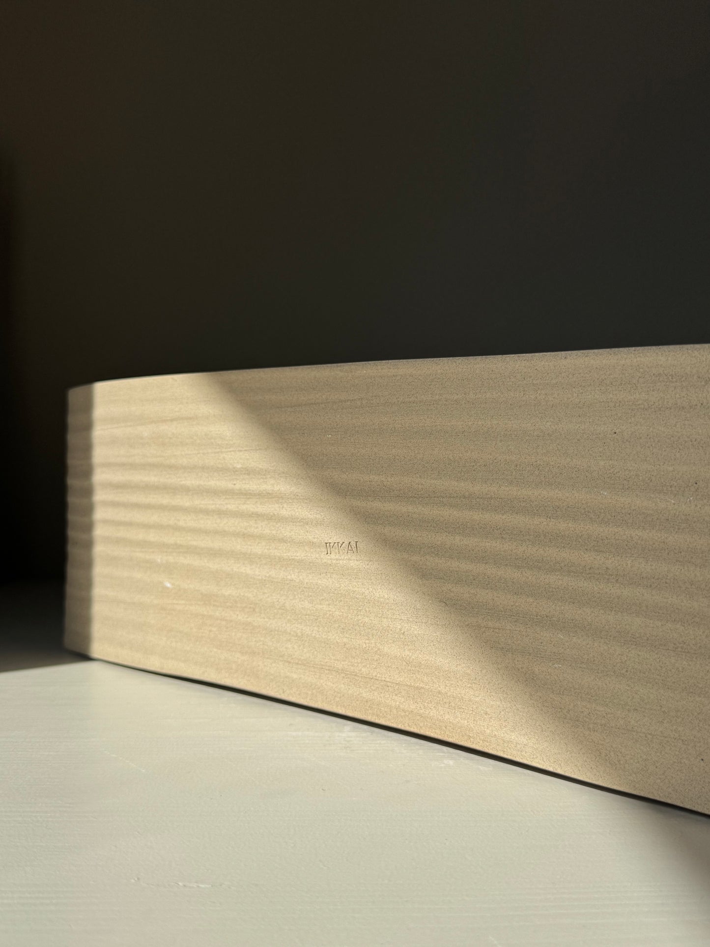 Sushi Plate – Inyo Series #03, handmade ceramic, highlighting unique soft curves and glazed finish on a shadowed surface.