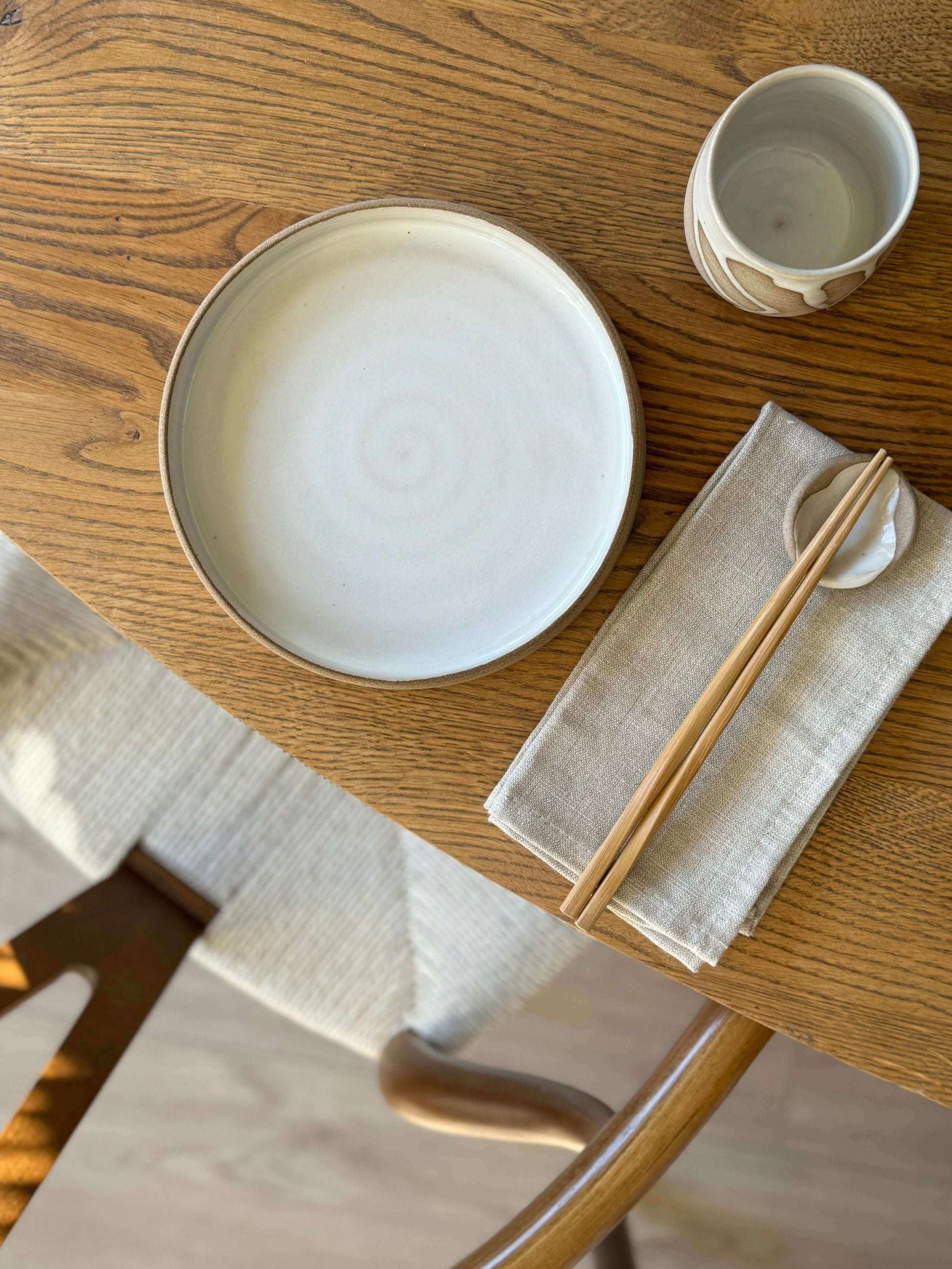 Yunomi Cups - Yuki on a wooden table with a white plate, napkin, and chopsticks, showcasing unique glaze drips over toffee clay.