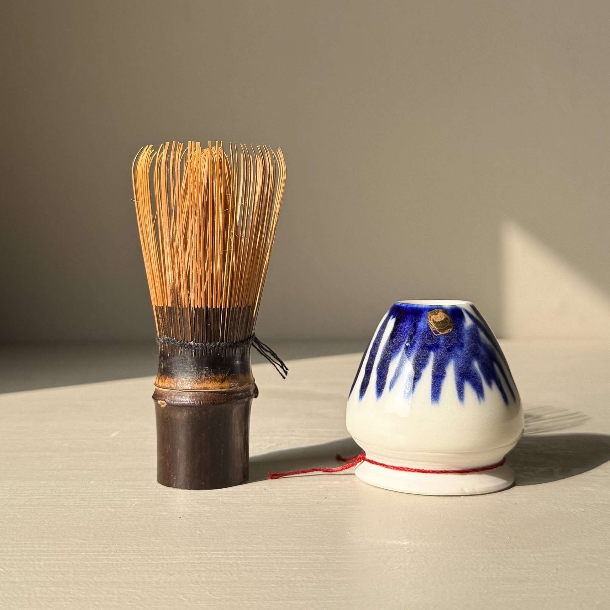 Porcelain Whisk Holder – Cobalt & Gold Lustre alongside a bamboo matcha whisk (chasen) on a light surface.