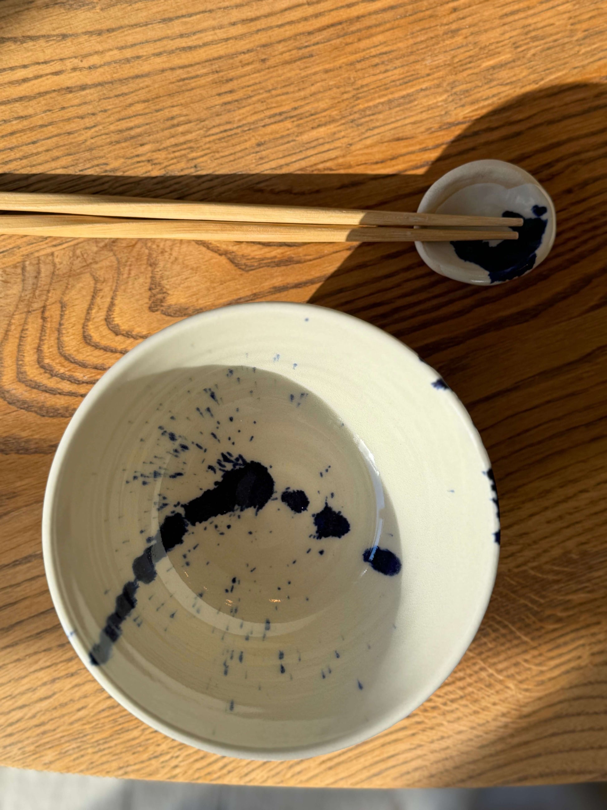 Rounded chopstick and matcha spoon rest in Gosu Series with cobalt blue splashes on wooden table, showcasing handmade craftsmanship.