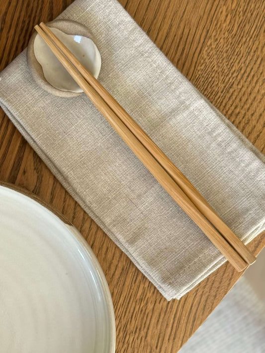 Rounded chopstick and matcha spoon rest from Yuki Series with soft curves and white glaze, placed on linen napkin for elegant dining.
