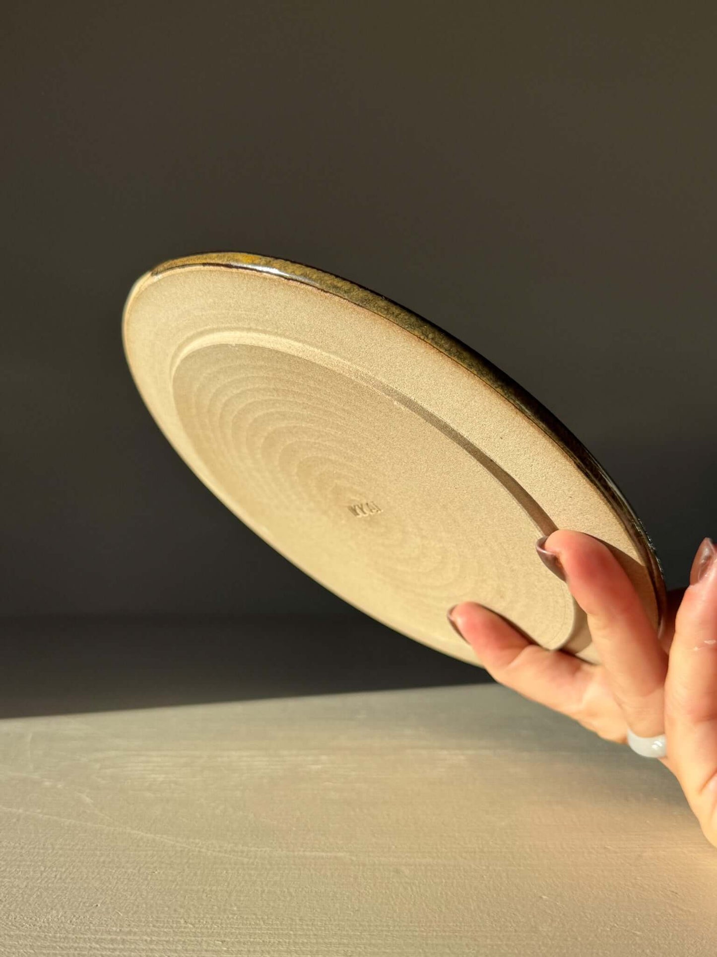 Hand holding a Side Plate – Inyo with natural finish, showing its detailed design and contrasting textures in warm tones.