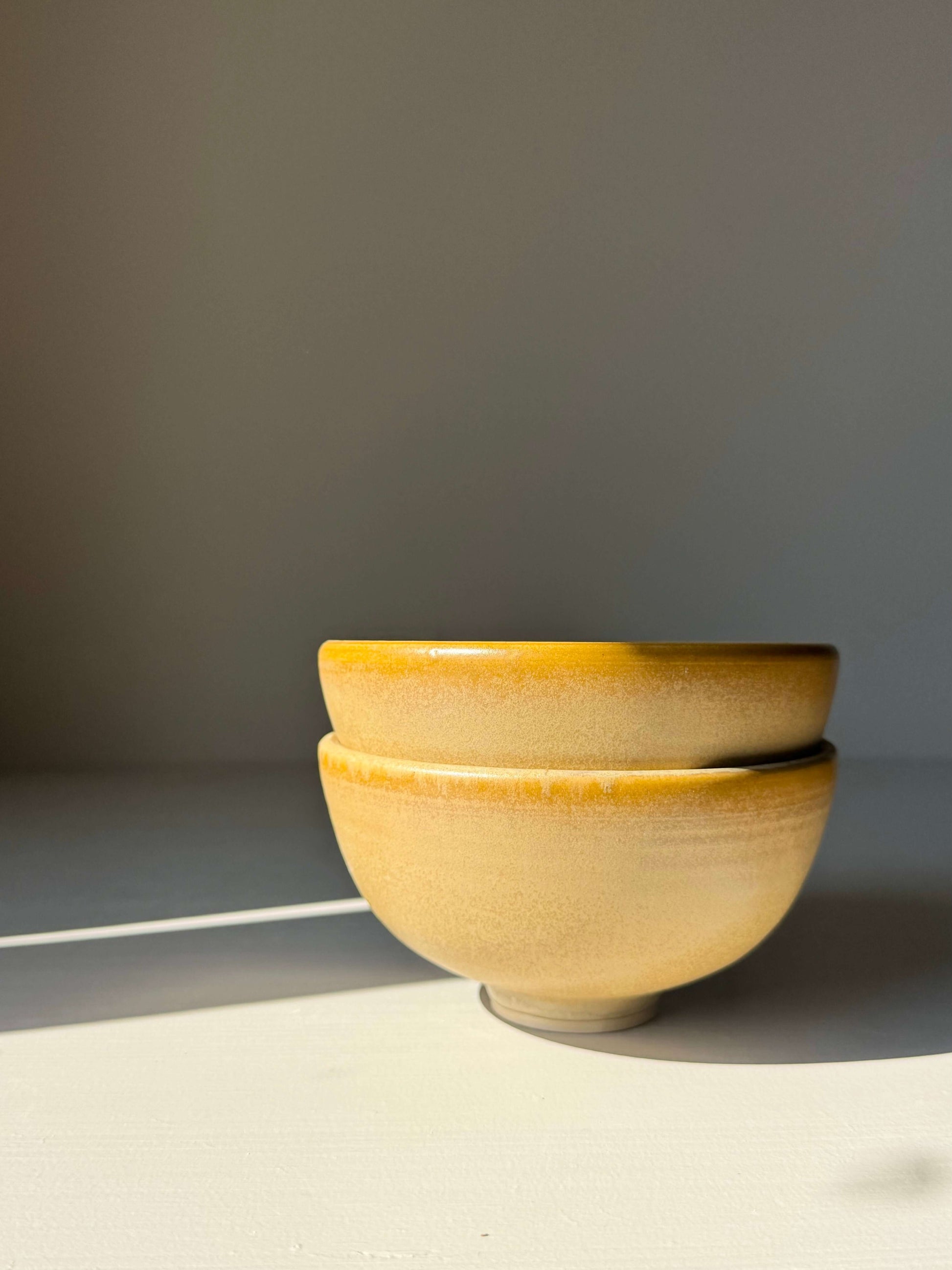 Stacked Small Bowl - Golden Yellow, handmade ceramic with soft ochre to honey glaze, sunlight highlights the subtle speckles and swirls.