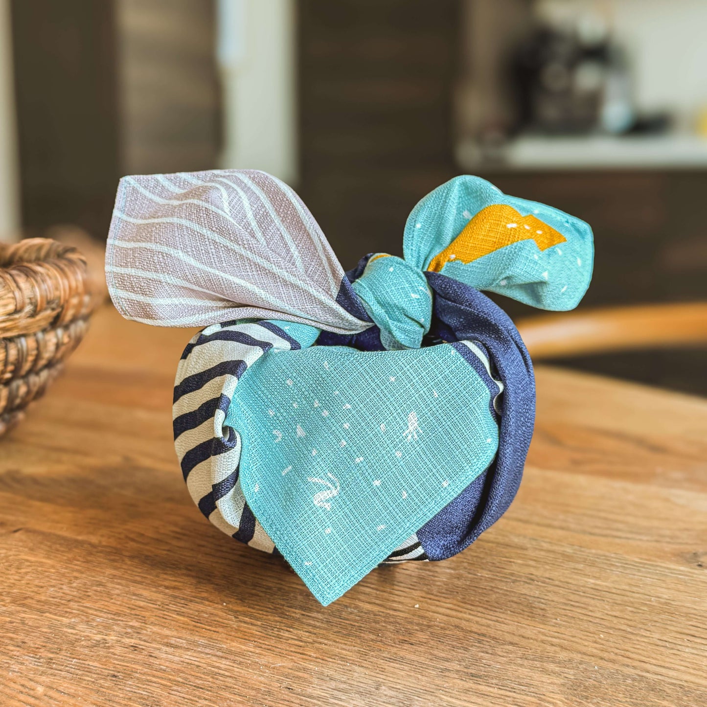 Small Furoshiki Blue Whale tied with playful fabric patterns on a wooden table.