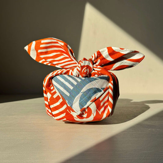 Small Furoshiki with Camellia orange and blue floral pattern, tied elegantly, showcasing Japanese elegance for wrapping and decor.