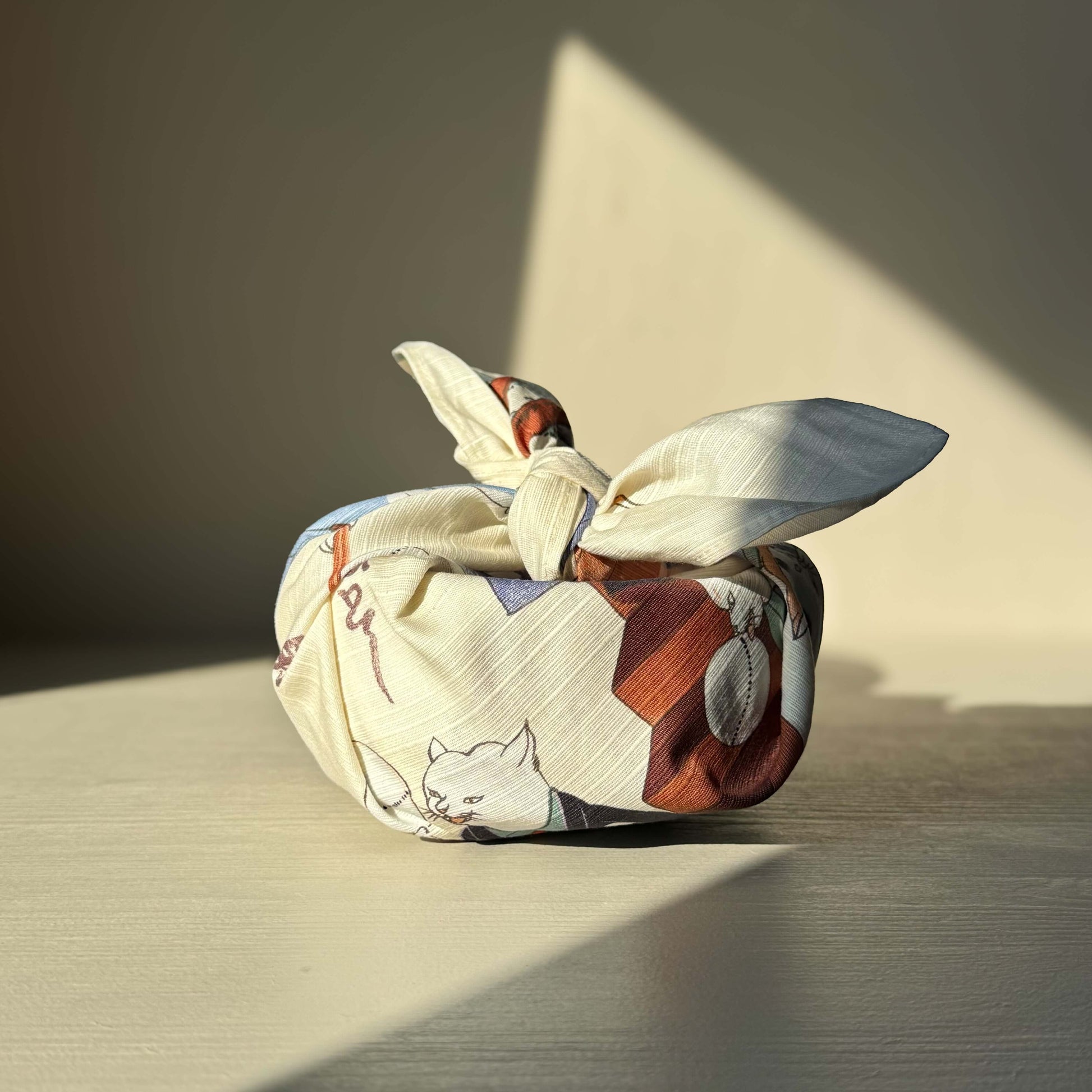 Small Furoshiki with 'Cats Juggling Balls' design on cream fabric, inspired by Utagawa Kuniyoshi, wrapped artfully.