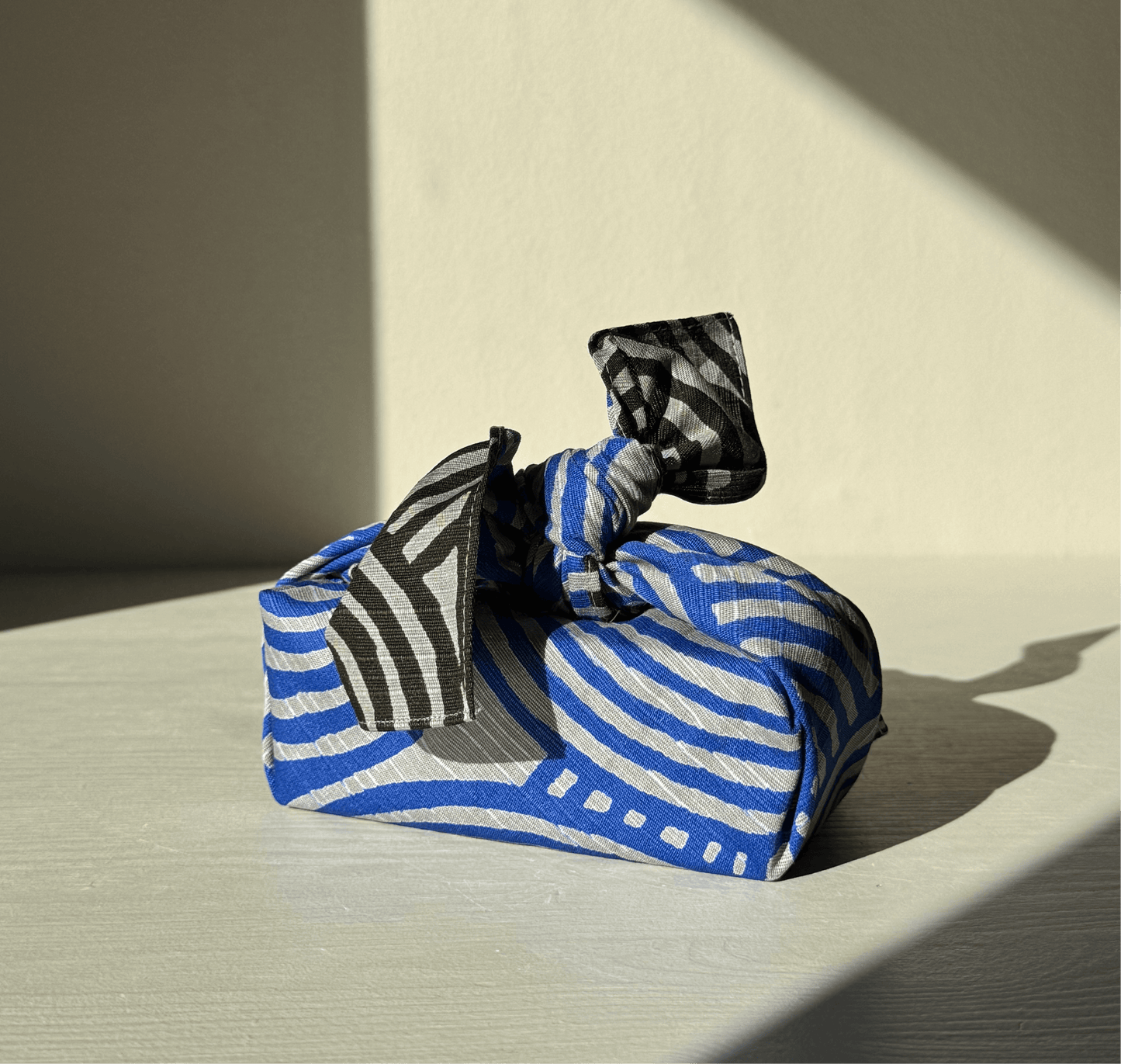 Small Furoshiki in dark gray and blue with a unique pattern, folded and tied, showcasing reusable wrapping design. Size: 48 cm x 48 cm.