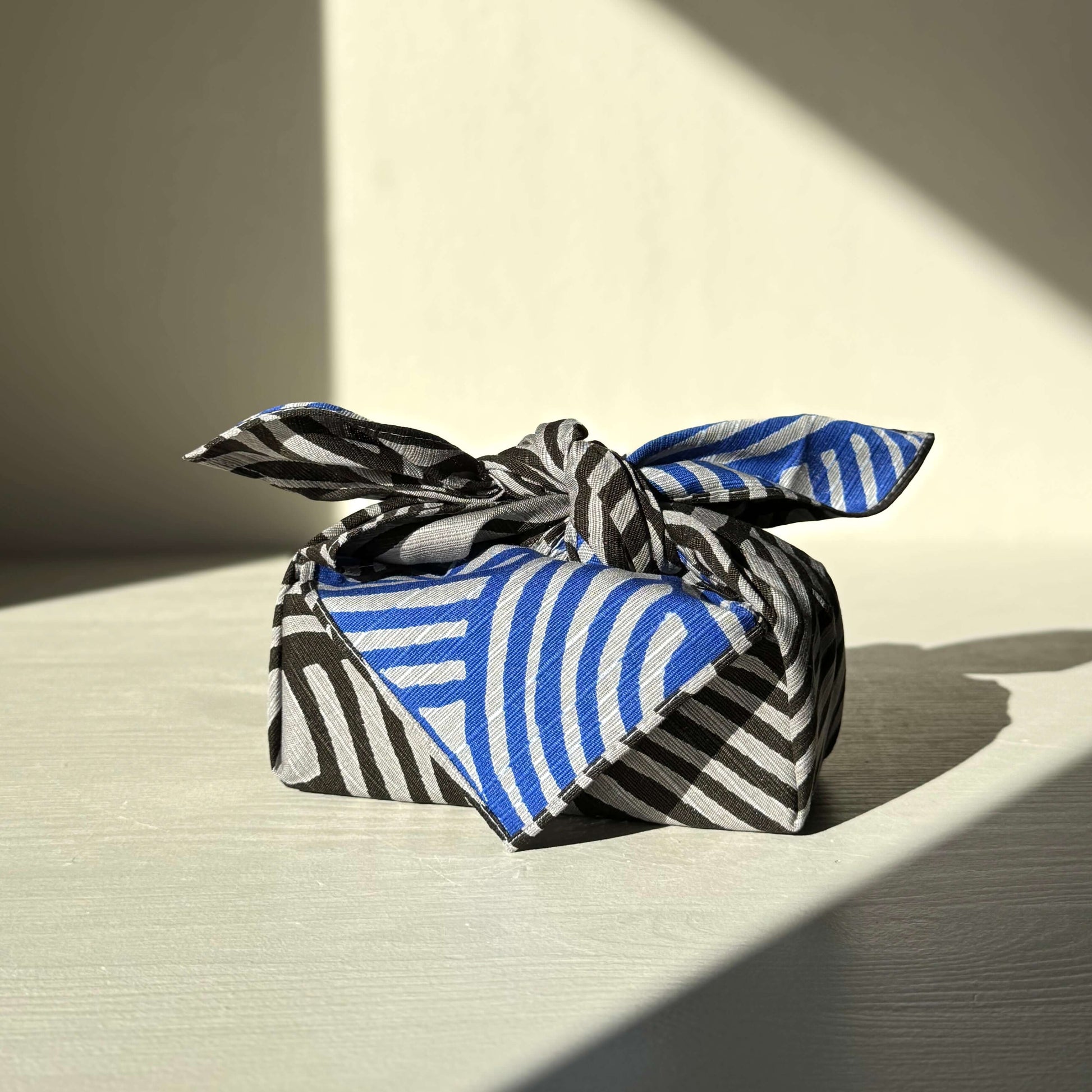 Small Furoshiki in dark gray and blue featuring Isa Monyo Connection design, tied in a stylish wrap, made from durable 100% cotton.