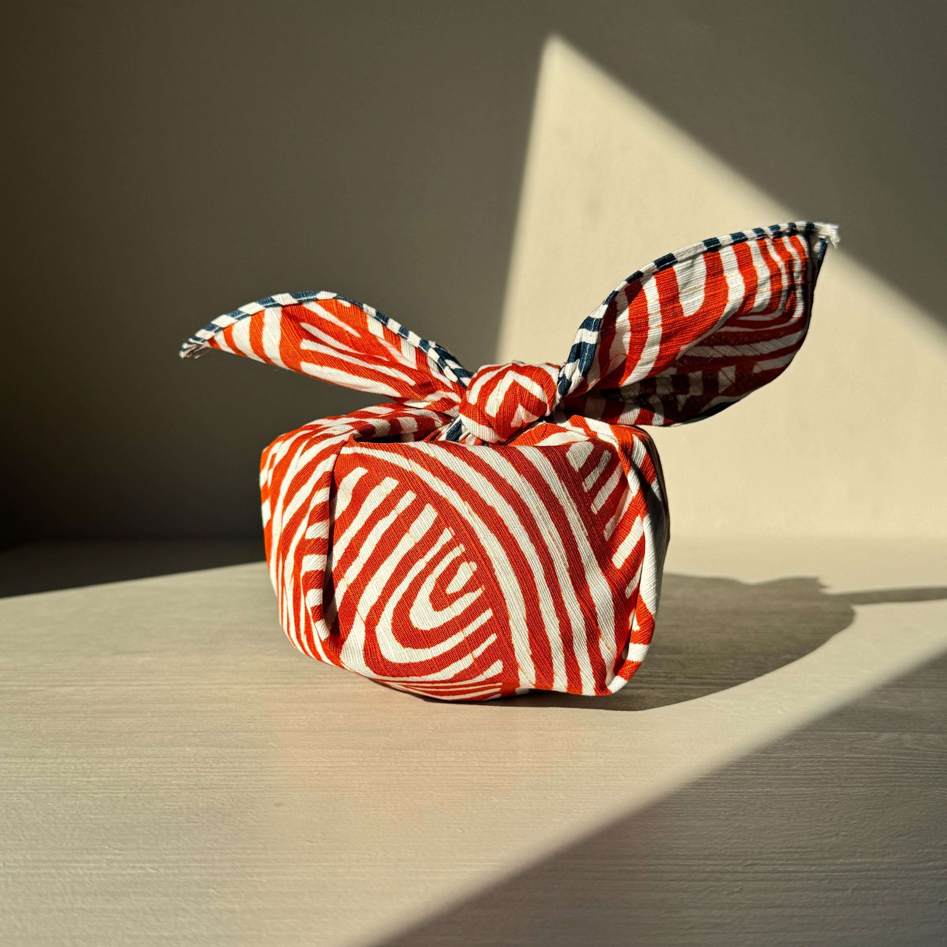 Small Furoshiki Isa Monyo Reversible Knot with flowing red and white pattern, symbolizing connection and harmony, beautifully wrapped.
