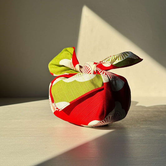 Red and green small furoshiki with plum blossom design, symbolizing happiness and resilience, used for wrapping gifts.