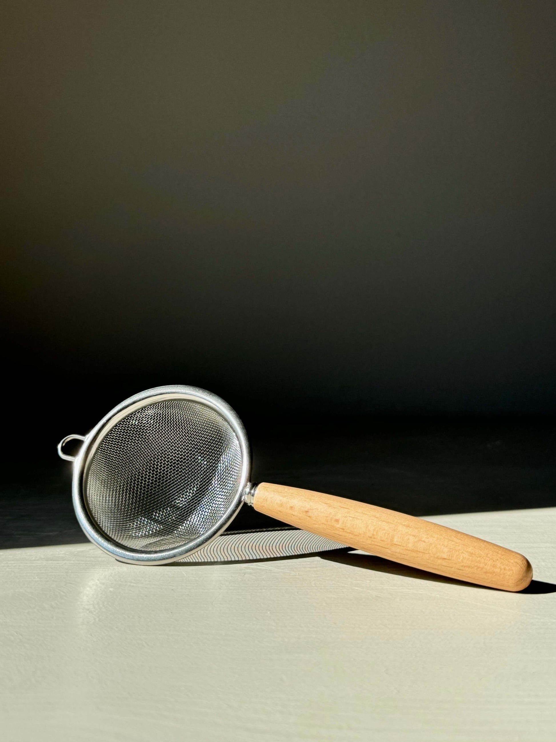 Stainless steel tea strainer with wooden handle, ideal for sifting matcha powder or loose leaf tea, shown on a neutral background.