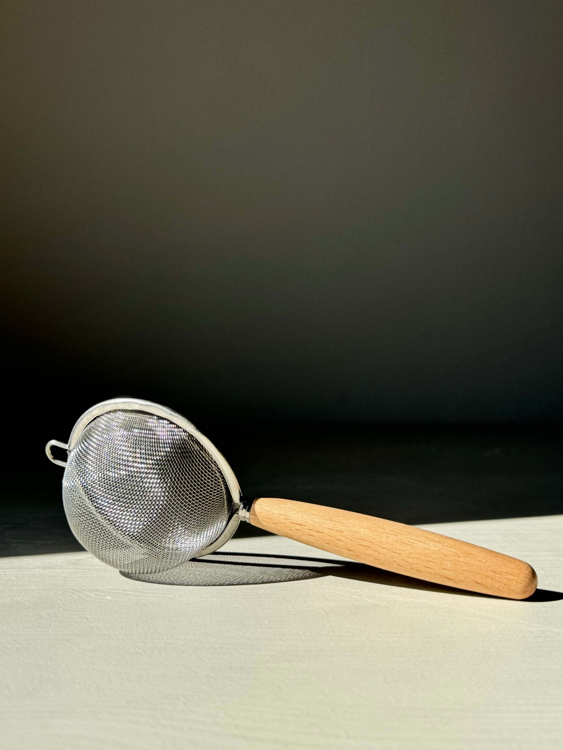 Stainless steel tea strainer with wooden handle for sifting matcha or loose leaf tea, featuring a finely woven mesh design.