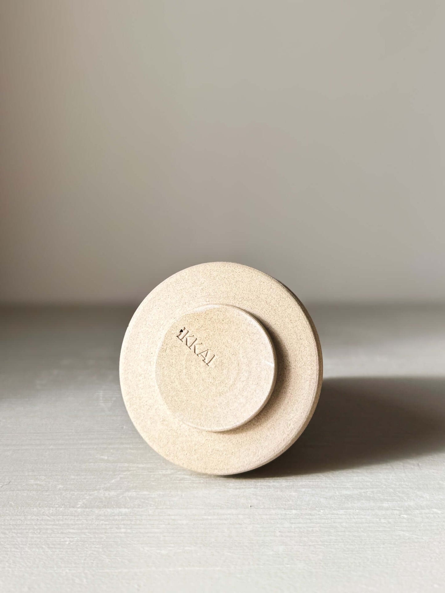 Close-up of a textured ceramic base with "HAKAI" text, minimalist design on a neutral surface, showcasing craftsmanship and detail.