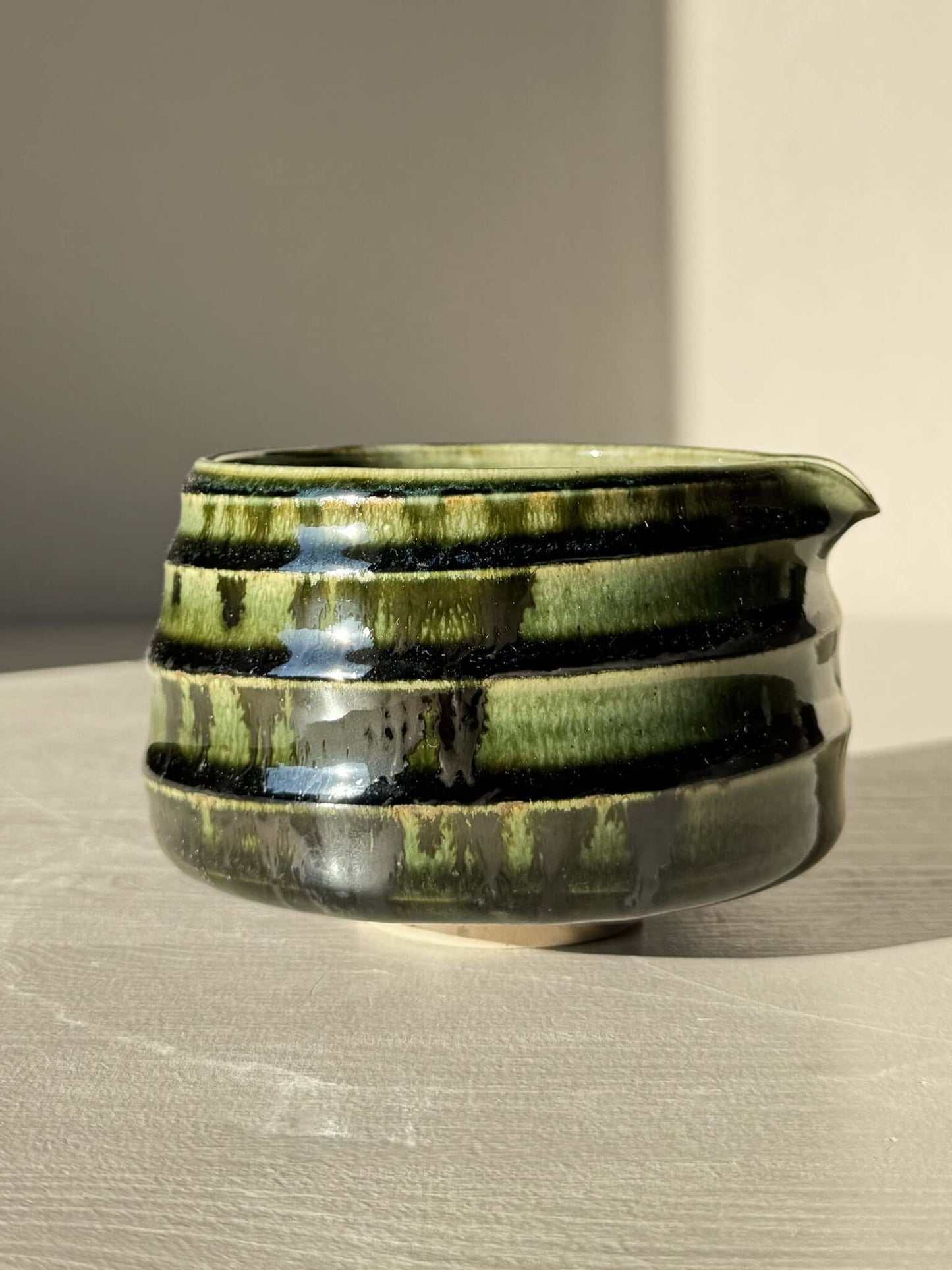 Textured Matcha Bowl Spout - Hinoki #04 with glossy green glaze, showing subtle ridges and a spout for easy pouring on a light surface.