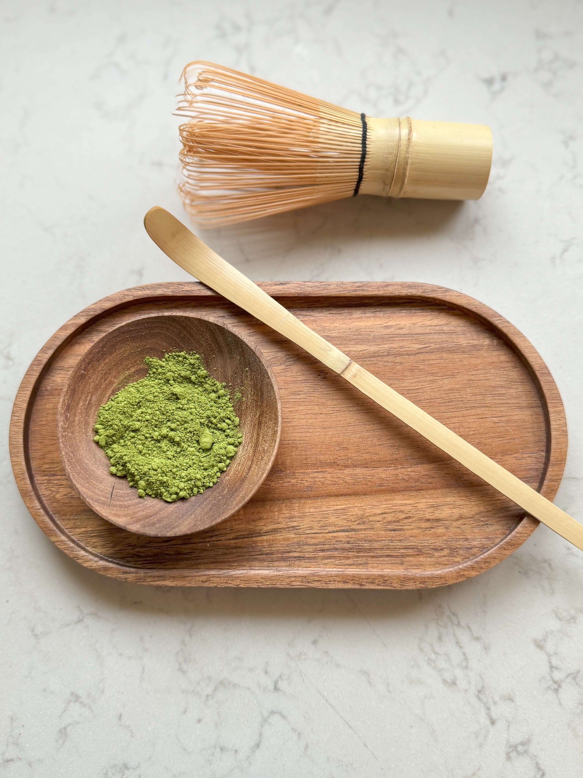 Traditional bamboo Chashaku matcha spoon on wooden tray with matcha powder and whisk.