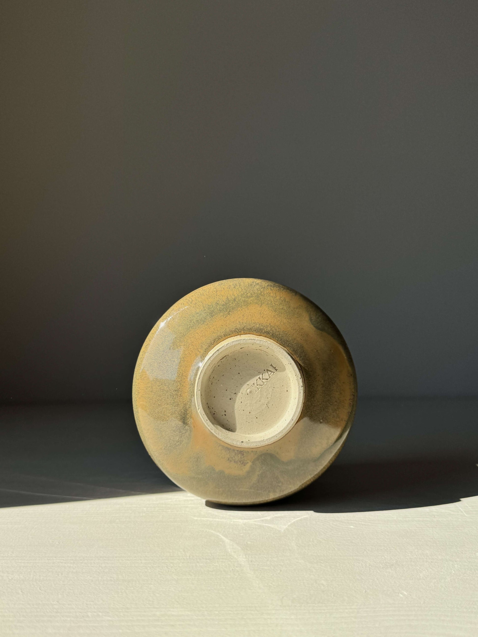 Bottom view of a Matcha bowl with spout, showcasing the tenmoku glaze shifting from rich brown to soft green in natural light.