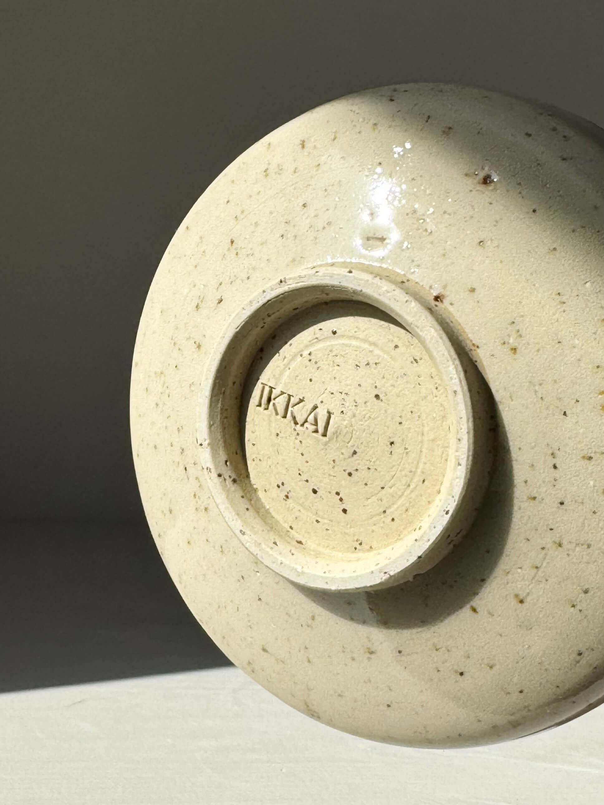 Base of a ceramic matcha bowl with subtle speckled design, highlighting the maker's mark "IKKAI" for artisanal craftsmanship.