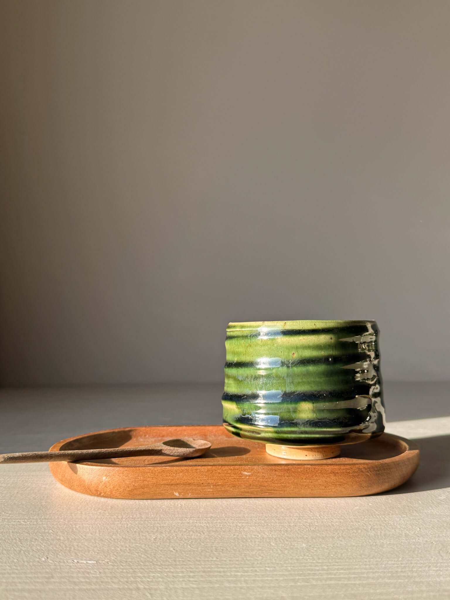 Yunomi Cup - Hinoki #10 with deep green glaze and hand-applied slip design on display with wooden tray and spoon.