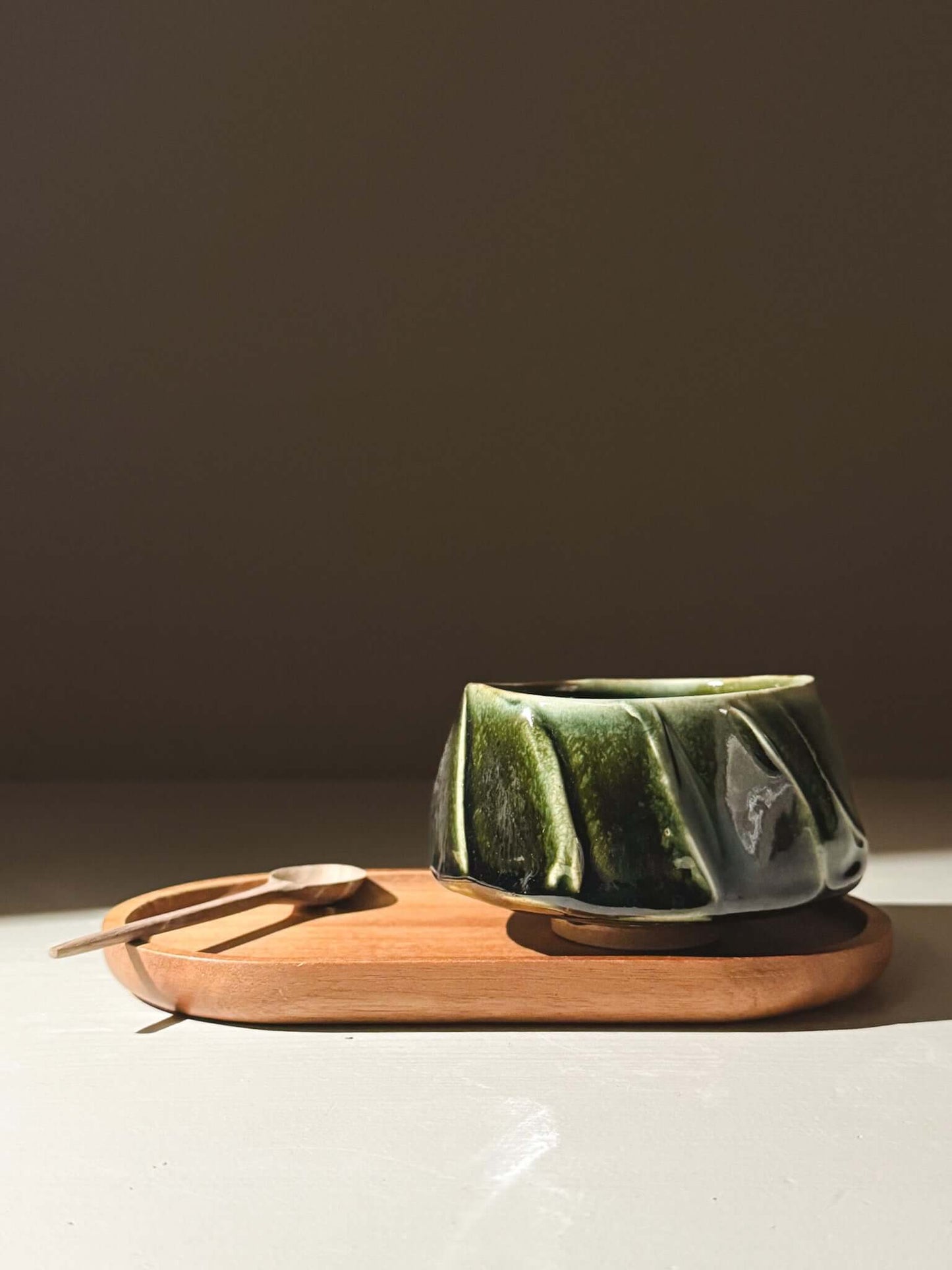 Yunomi Cup - Hinoki #00 with deep green glaze on a wooden tray, showcasing its unique hand-decorated slip texture and subtle elegance.