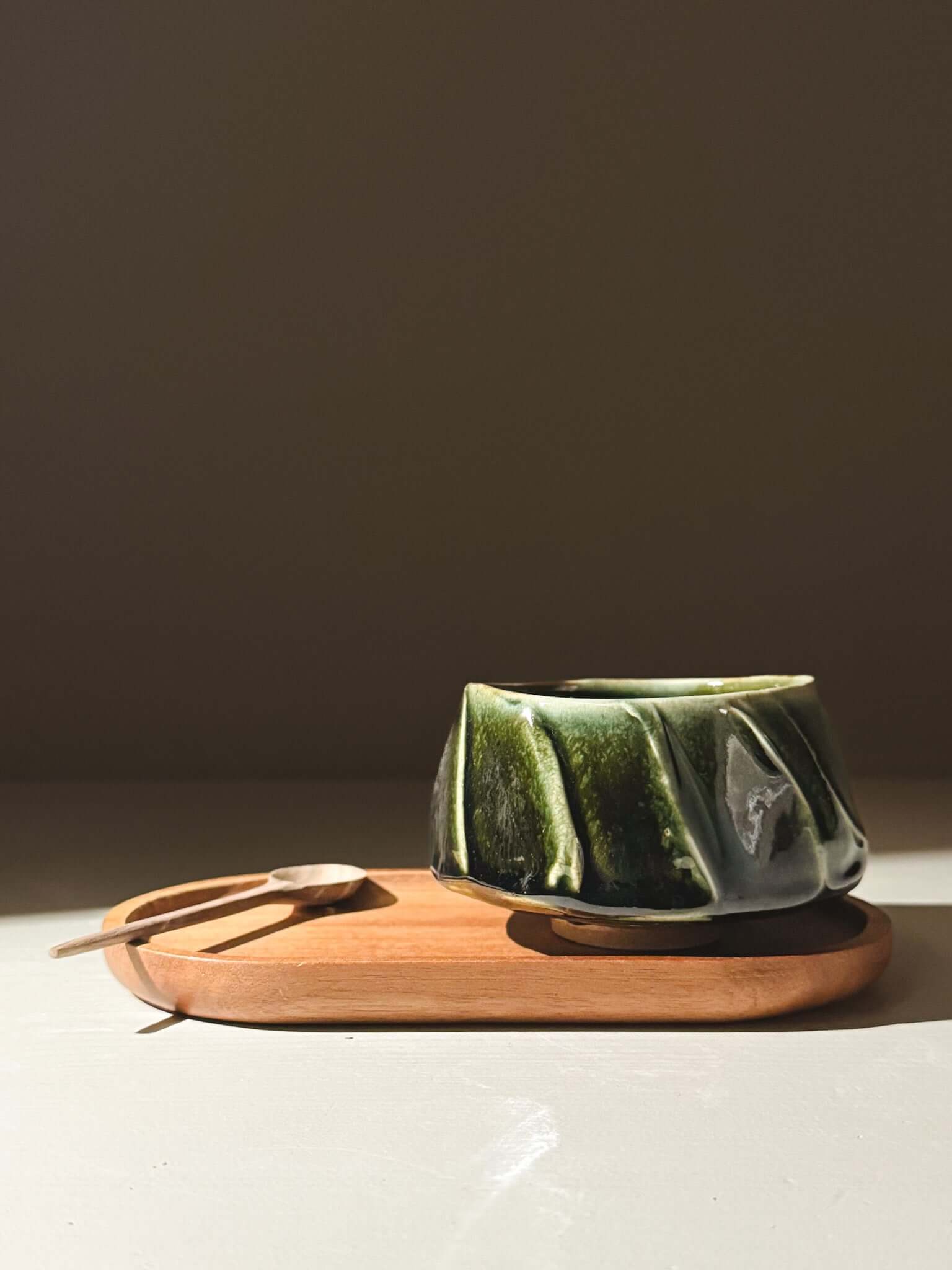 Yunomi Cup - Hinoki #00 with deep green glaze on a wooden tray, showcasing its unique hand-decorated slip texture and subtle elegance.