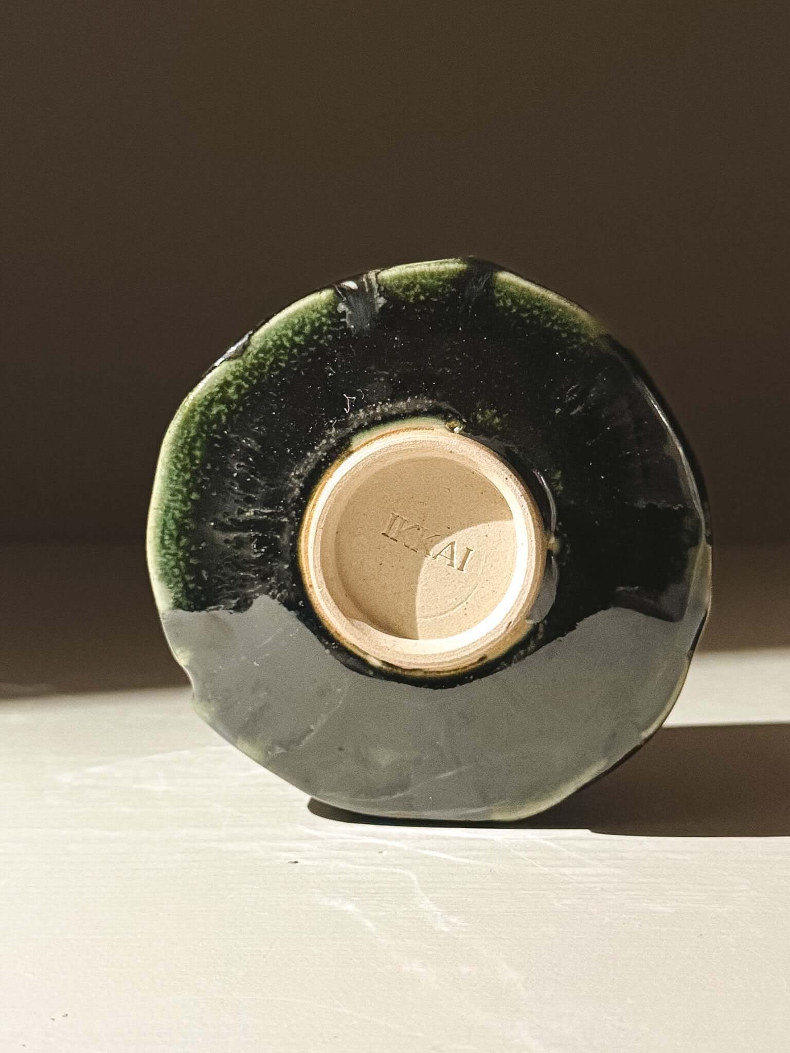 Bottom view of Yunomi Cup - Hinoki #00, showcasing handmade subtle texture and deep green glaze with unique slip patterns.