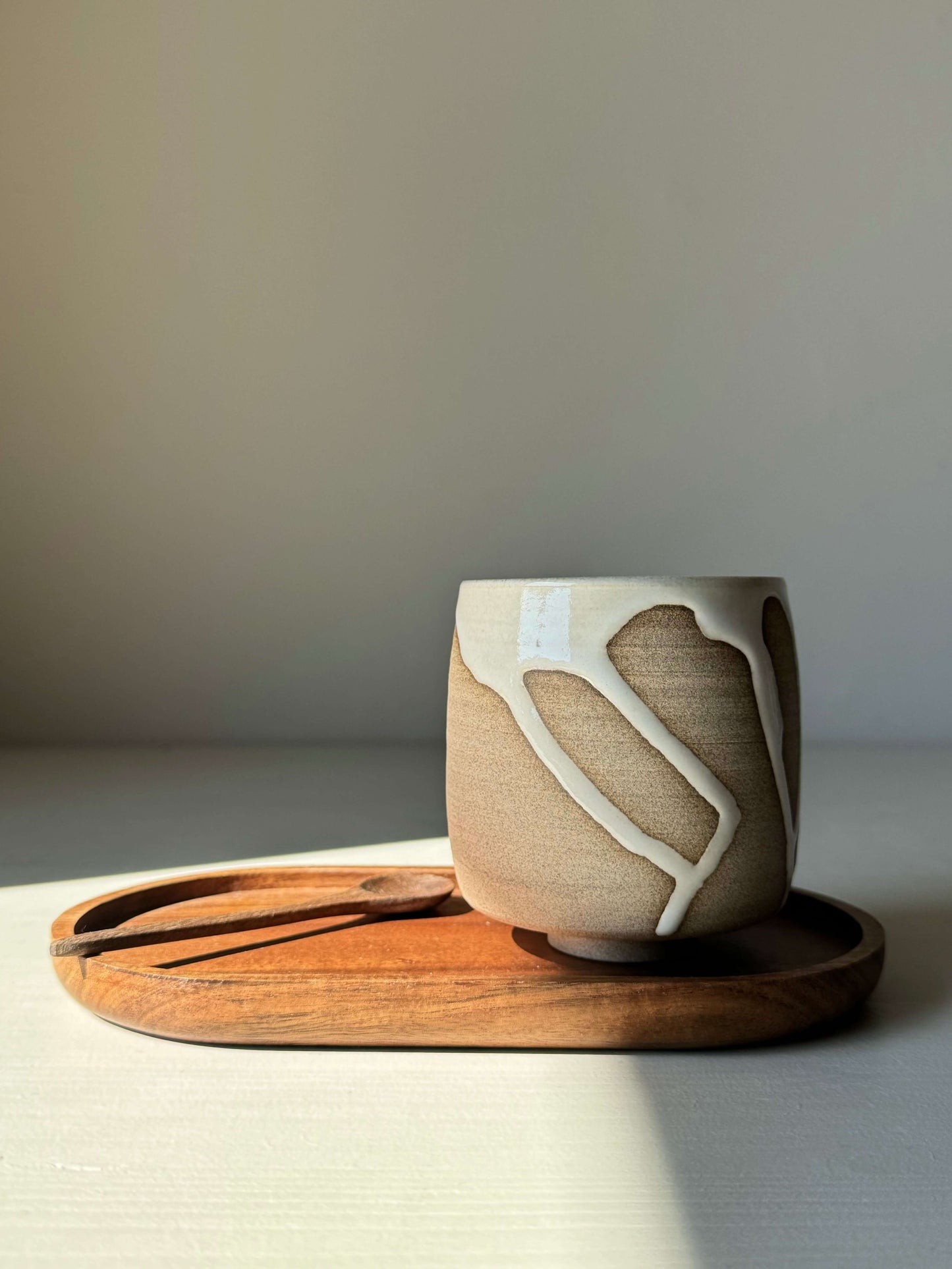 Yunomi cup from the Yuki Series with white glaze over toffee clay on a wooden tray, showcasing unique drips and quiet balance.