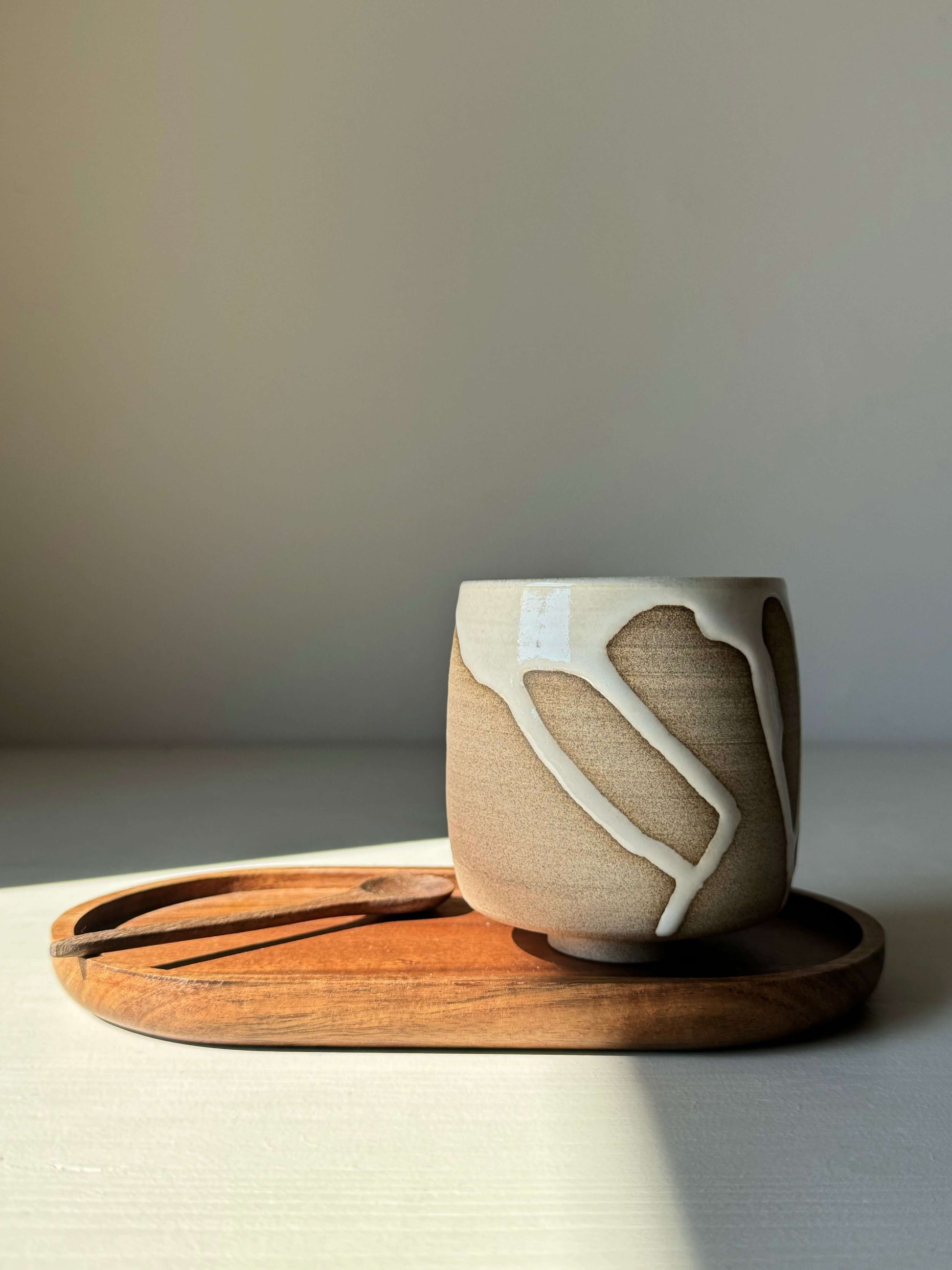 Yunomi cup from the Yuki Series with white glaze over toffee clay on a wooden tray, showcasing unique drips and quiet balance.