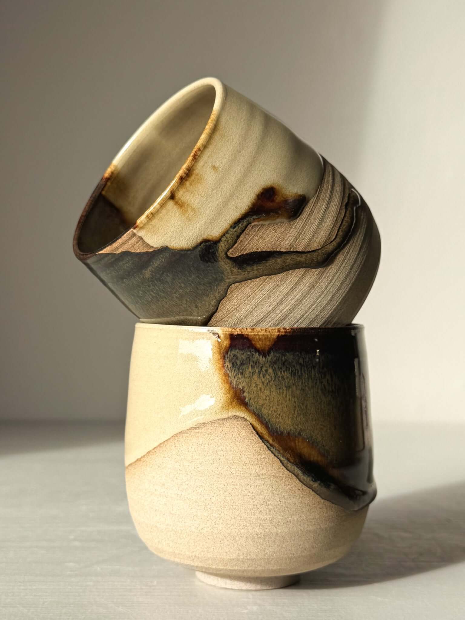Yunomi Cups - Inyo with dark tenmoku and clear glaze over toffee clay, showcasing a contrast of glossy and natural textures.