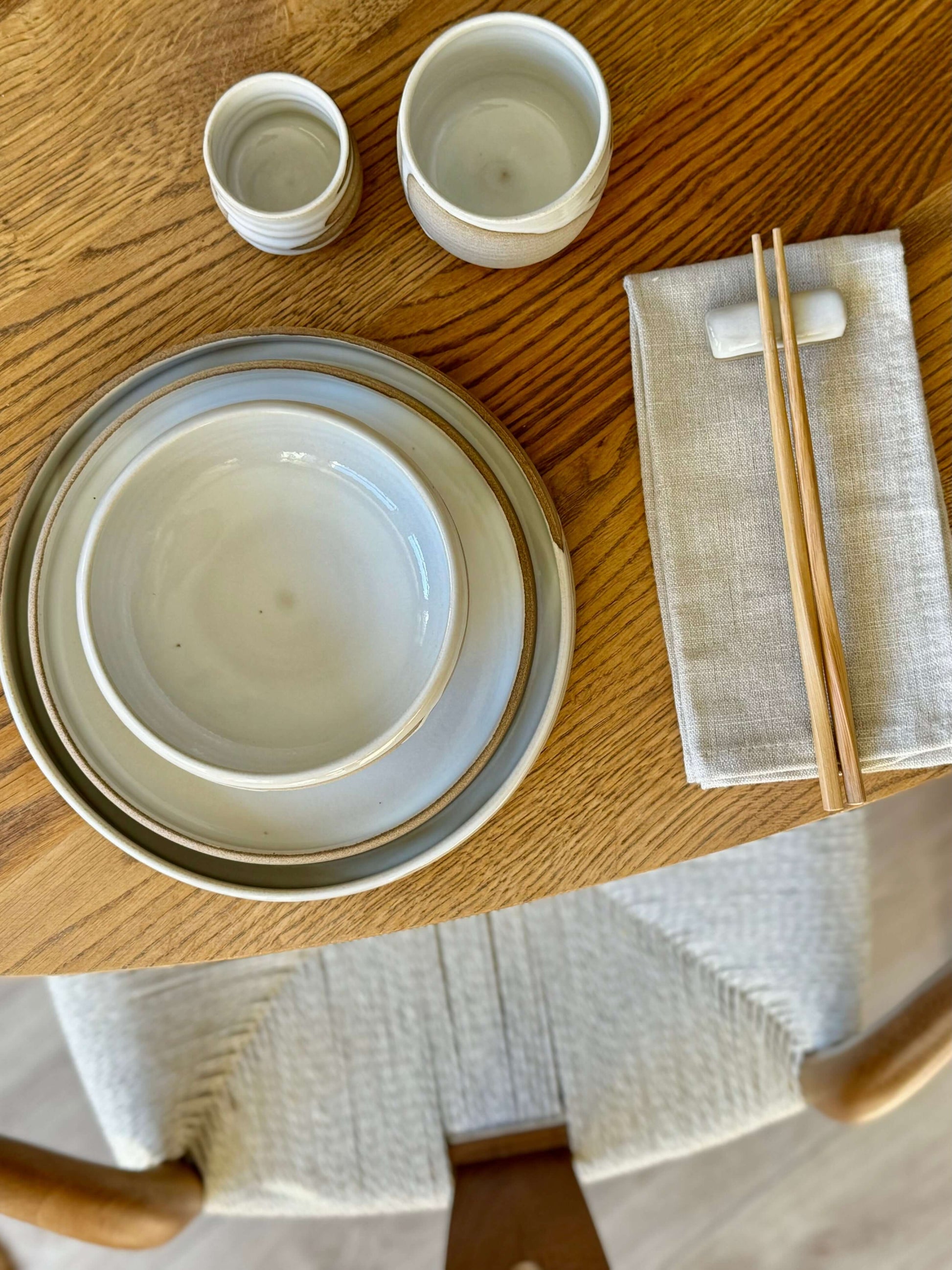 Yunomi cups from Yuki Series with toffee clay and white glaze on a wooden table, alongside plates, napkin, and chopsticks.