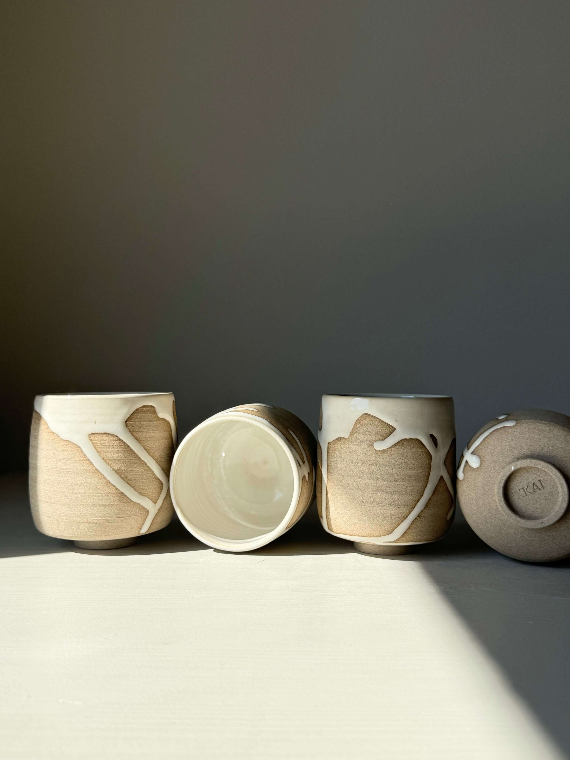 Yuki Series Yunomi Cups with soft white glaze over toffee clay, showcasing unique drips and textures, in soft lighting.