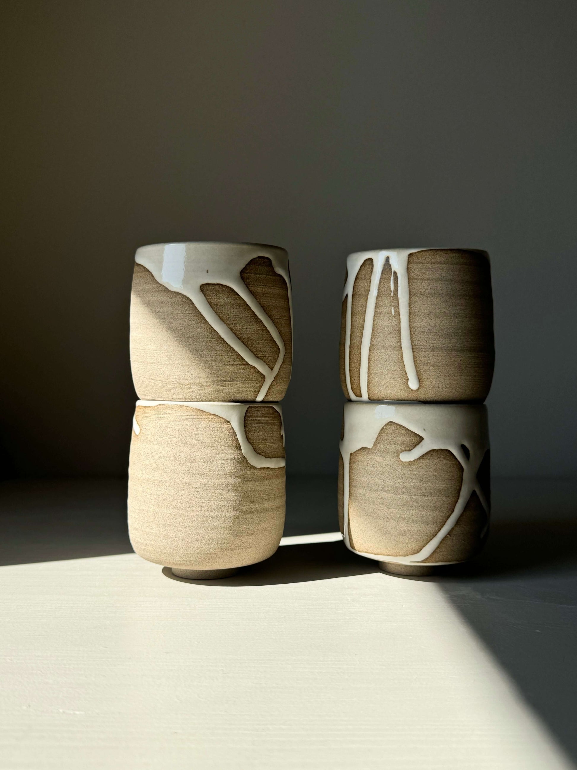 Alt Tag: Yuki Series yunomi cups with flowing white glaze on toffee clay, showcasing unique drips and textures, stacked on a table.