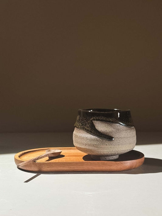 Yunomi Cup - Kuro Ash #02 on a wooden tray, showcasing its grey stoneware and glossy black glaze with natural movement.