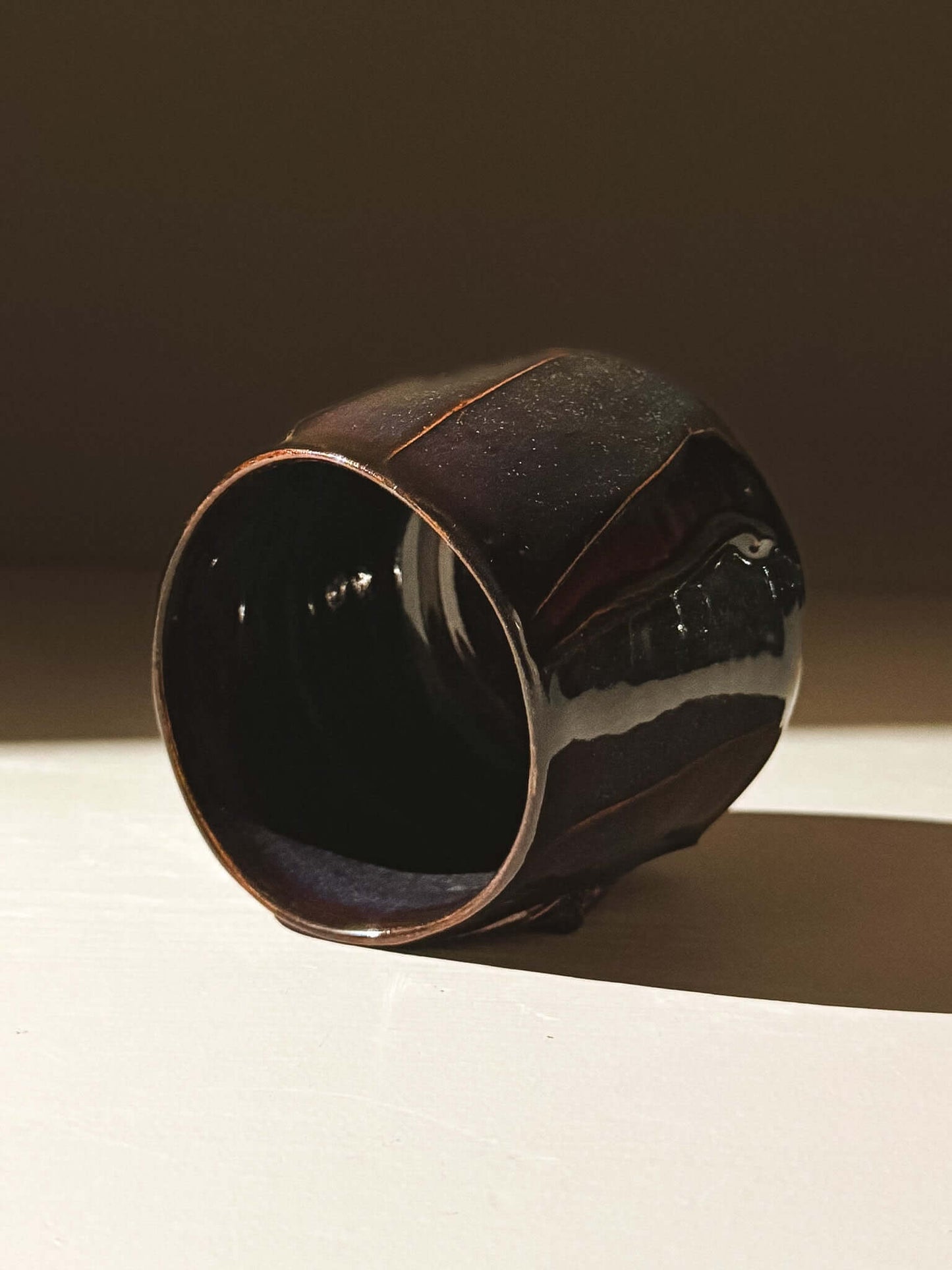 Yunomi Cup - Kuro with glossy black glaze revealing deep blue, burgundy, and red hues in light, showcasing its handmade detail.