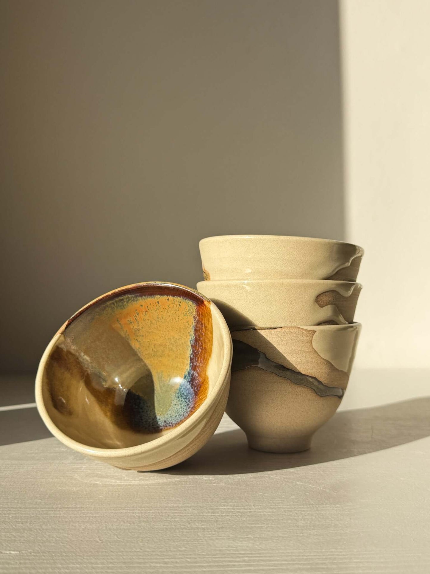 Set of Yunomi Cups - Inyo #01 in soft, flowing glaze with unique colors of gold, brown, blue, and green, stacked on a light surface.